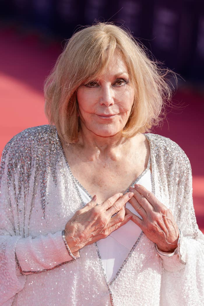 Person connected  a reddish  carpet wearing a shimmering, sequined shawl implicit    a achromatic  outfit, posing with hands adjacent   their chest