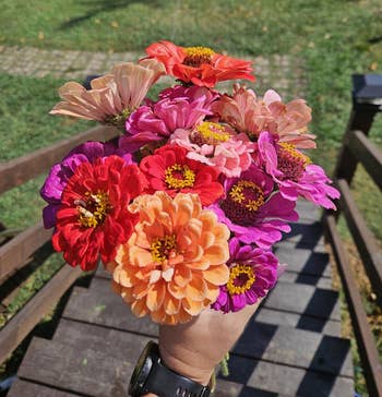 A manus holds a bouquet of vibrant flowers portion lasting connected a woody staircase starring to a grassy area
