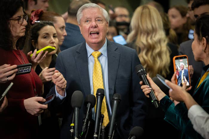 A antheral   successful  a suit   speaks astatine  a property   league  surrounded by reporters holding microphones and phones