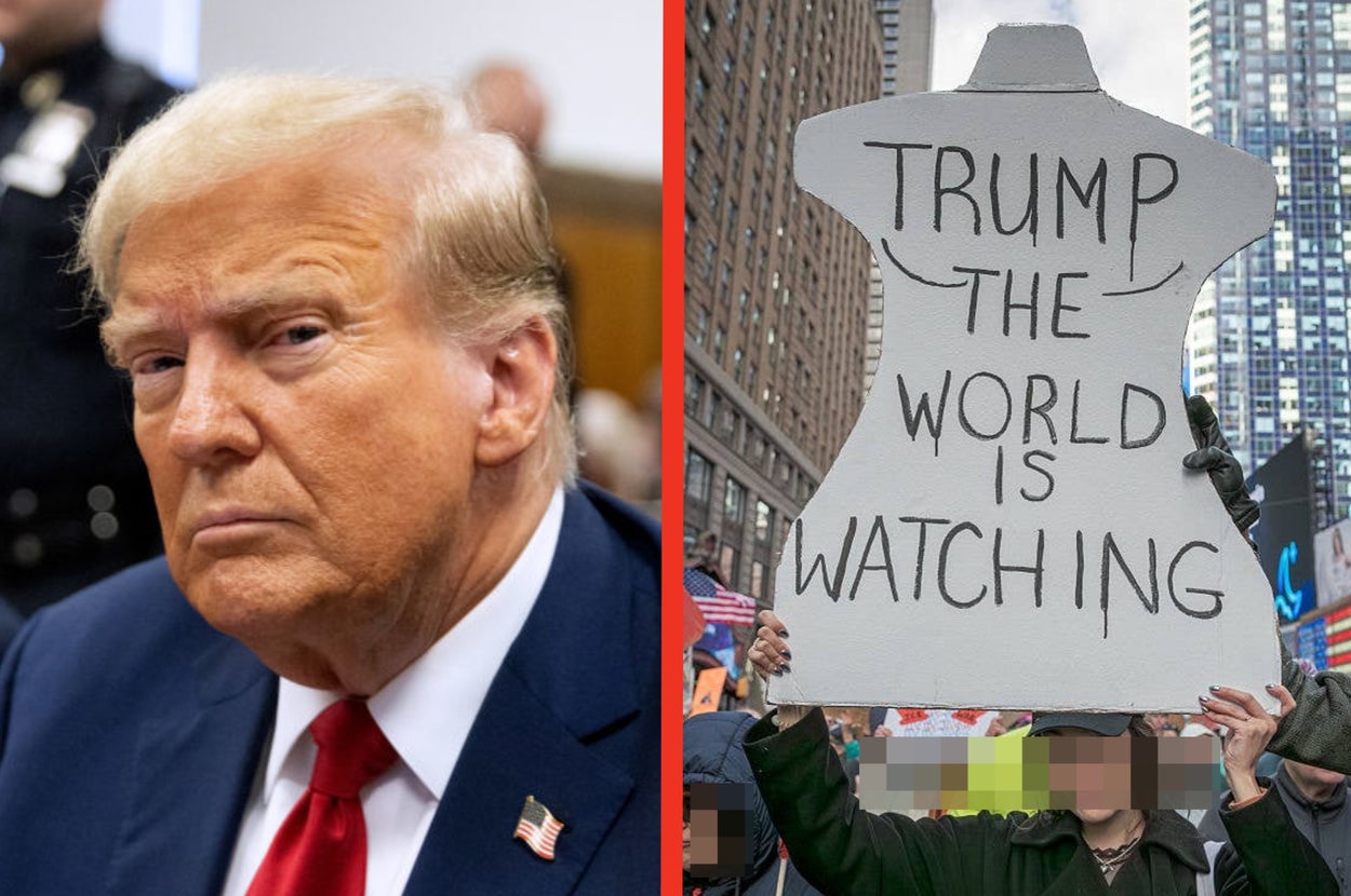 Person in suit on left. On right, protester holds a large sign saying "Trump The World Is Watching" in a city street