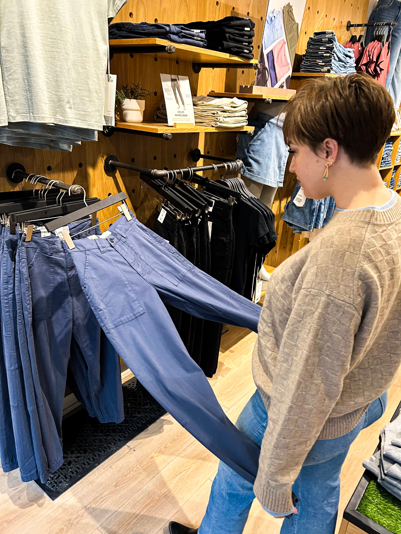 Person browsing bluish  pants successful  a covering  store, examining cloth  connected  rack with folded shirts successful  background