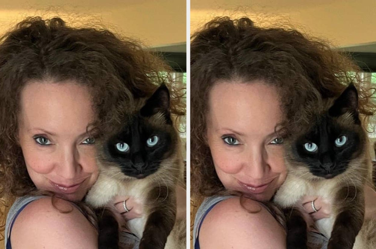 Person smiling while holding a Siamese cat close to their face. Both have matching expressions