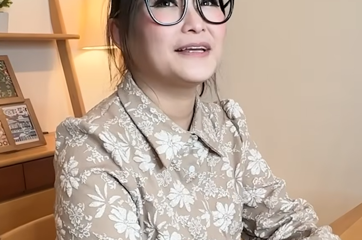 女性が室内で眼鏡をかけ、花柄の服を着て座っています。字幕には「自分が寝ちゃうやん！」と書かれています。