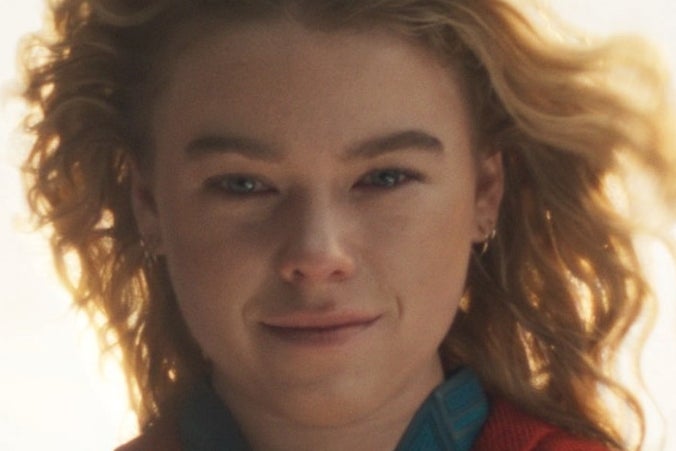 Person in superhero costume with 'S' emblem, cape flowing, standing confidently against a bright sky