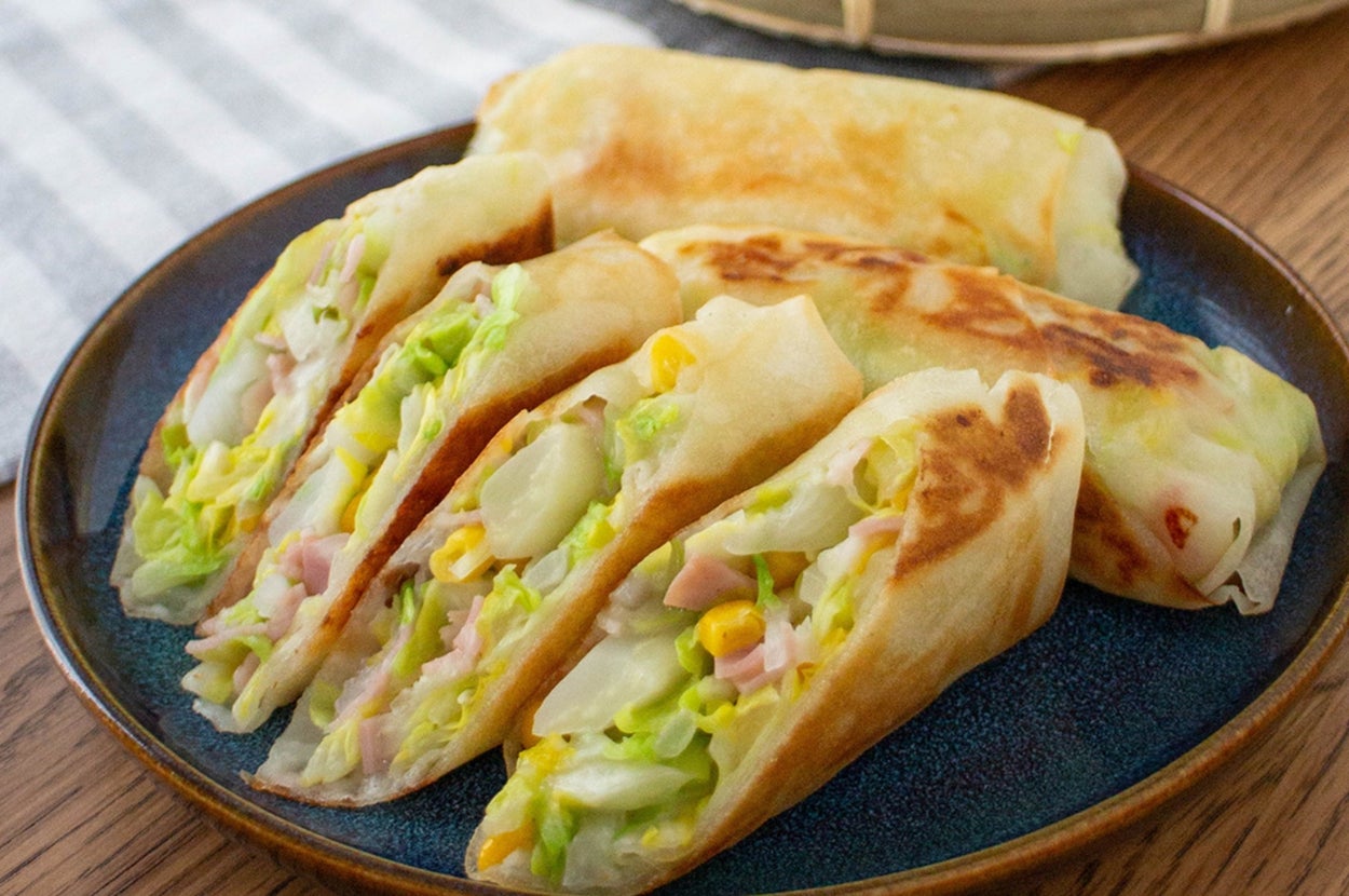 お皿に盛られた春巻きの断面。キャベツやコーンが見える。後ろに玉ねぎとレタスが置かれている。