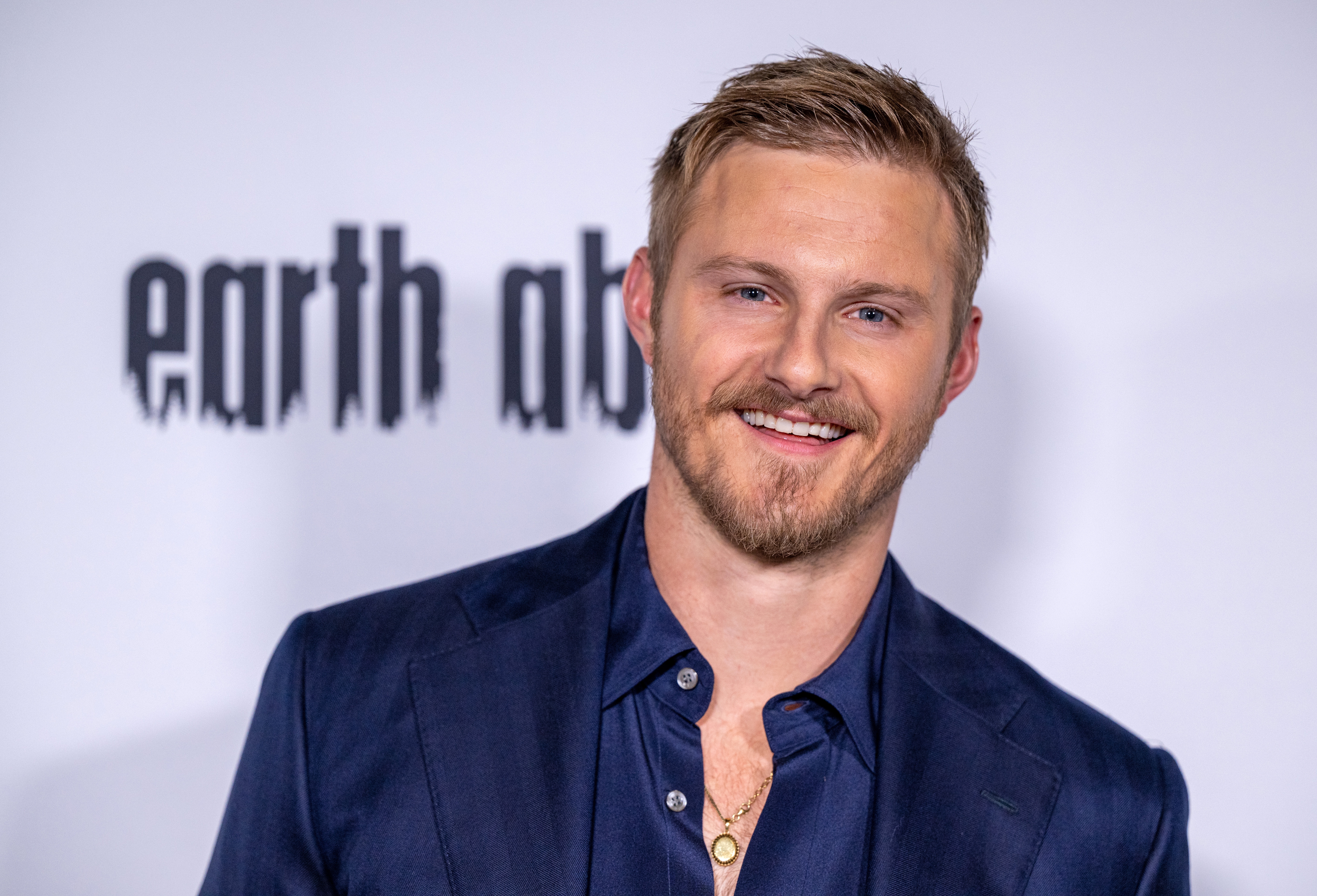 Man successful a suit smiles astatine a media event, lasting successful beforehand of a backdrop with text