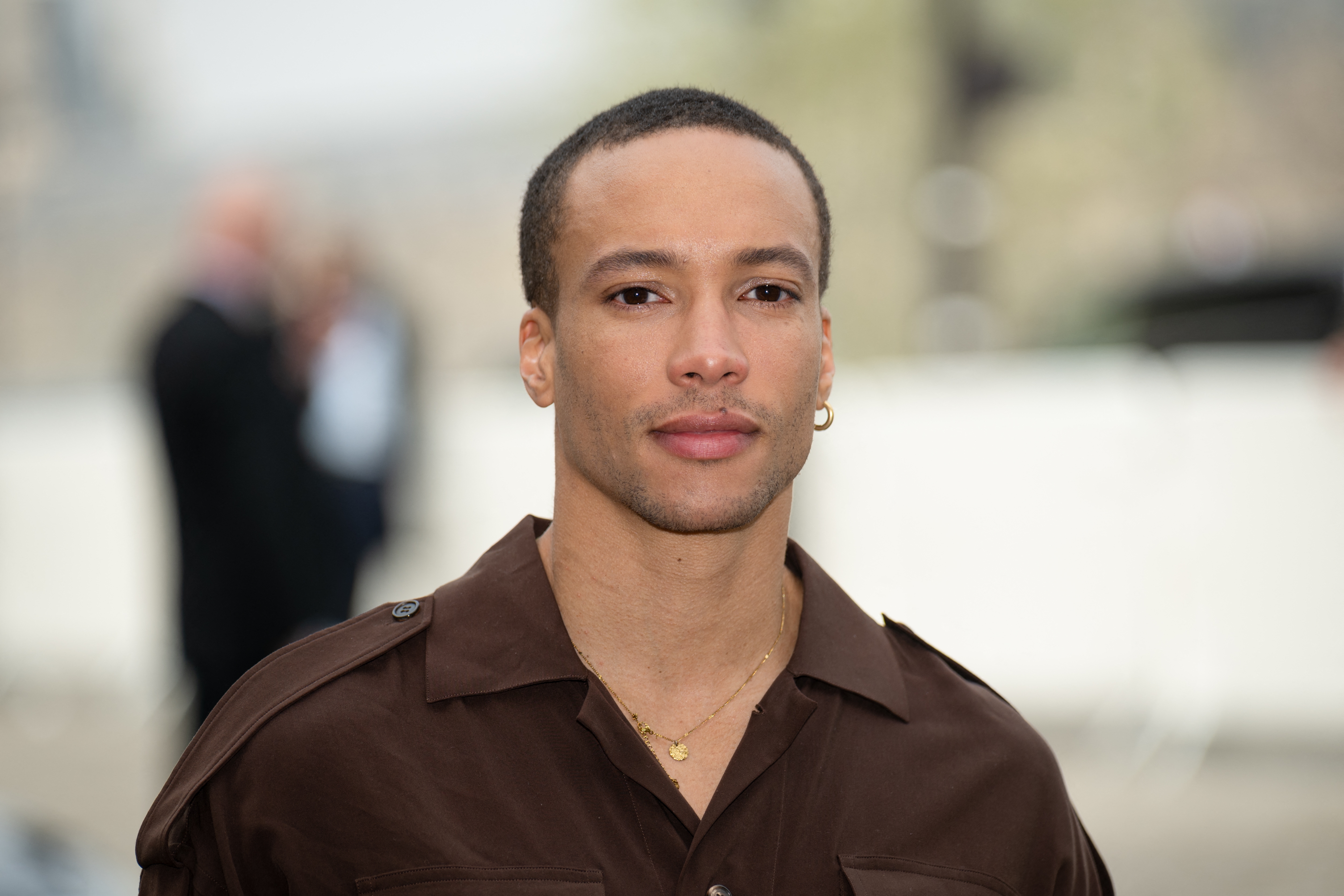 Person successful a acheronian overgarment with abbreviated hair, looking into the camera astatine an outdoor event. Blurred background
