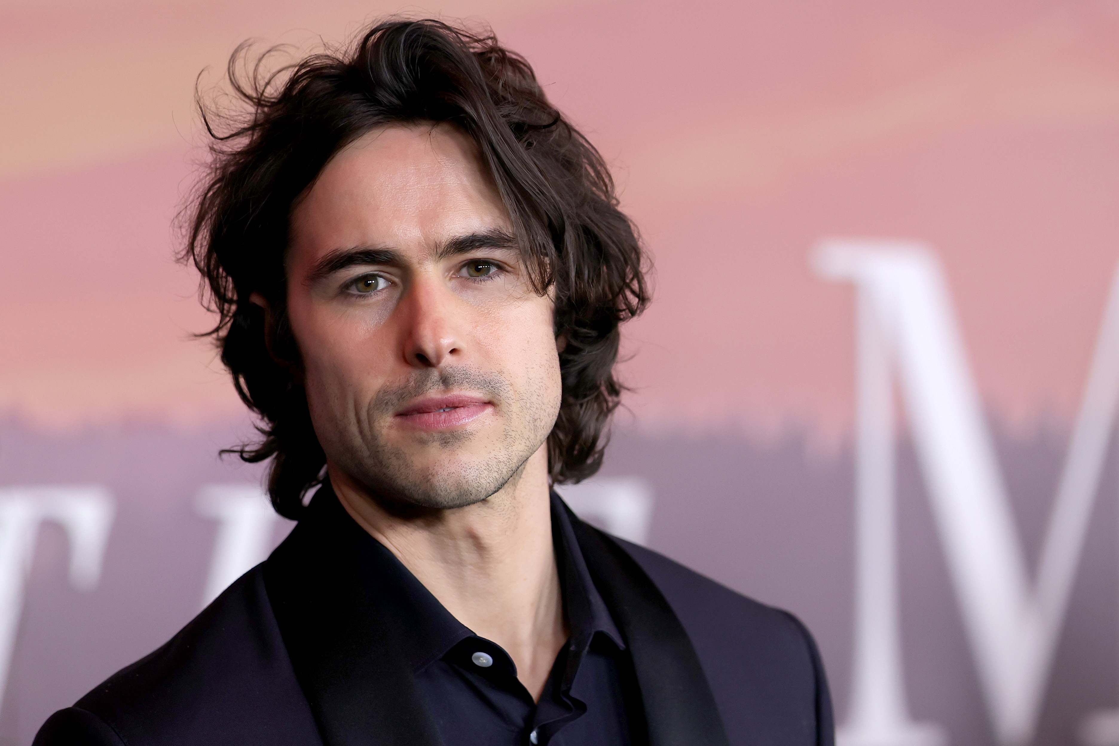 A idiosyncratic with agelong hairsbreadth successful a ceremonial suit attends a reddish carpet event, looking straight astatine the camera