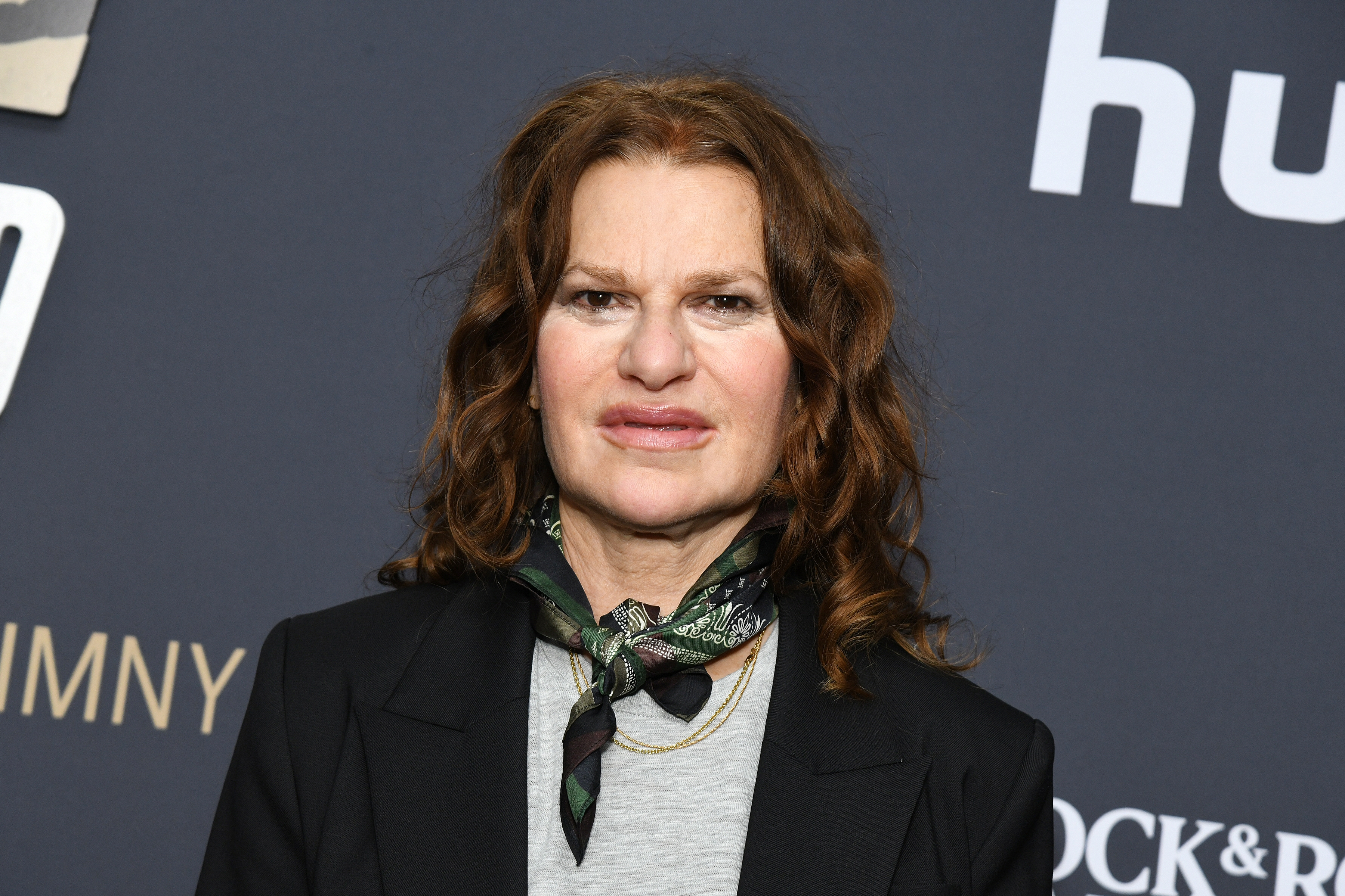 Person successful a suit overgarment and scarf astatine an event, lasting successful beforehand of a backdrop with text