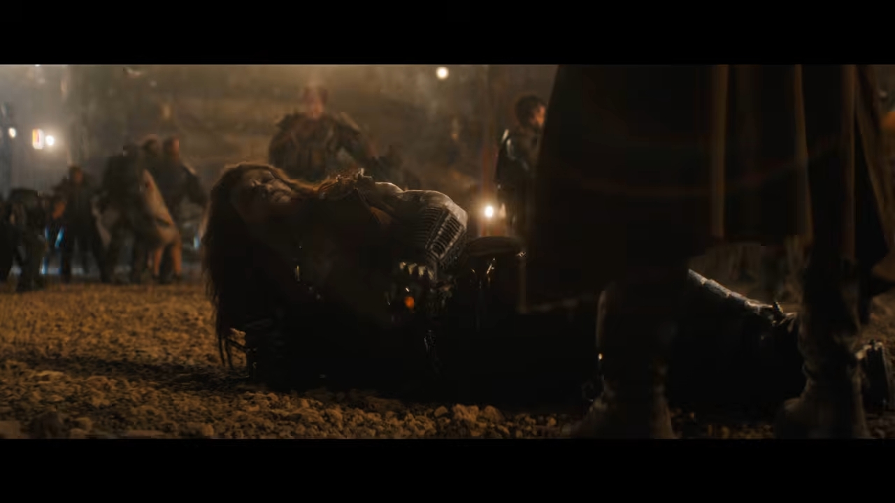 A dramatic scene from an action movie shows a person in armor lying on the ground amidst chaos