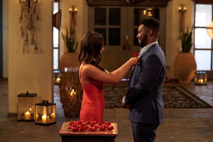 A pistillate   successful  a lace formal  pins a roseate  connected  a antheral   successful  a suit, lasting  successful  a country   with candles and a array  covered with roses