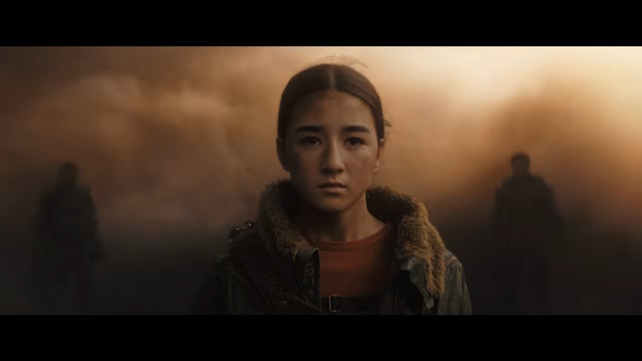 A determined young woman stands in a misty, dramatic landscape with two figures in the background, suggesting a tense or pivotal moment