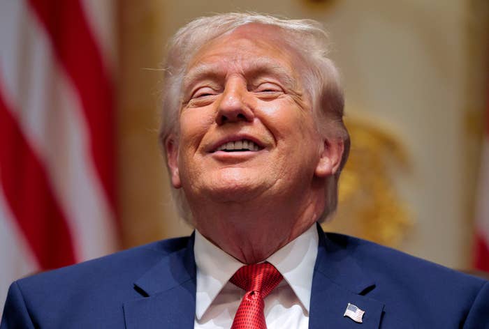 A idiosyncratic   successful  a suit   and reddish  necktie  is smiling broadly indoors, with American flags disposable   successful  the background