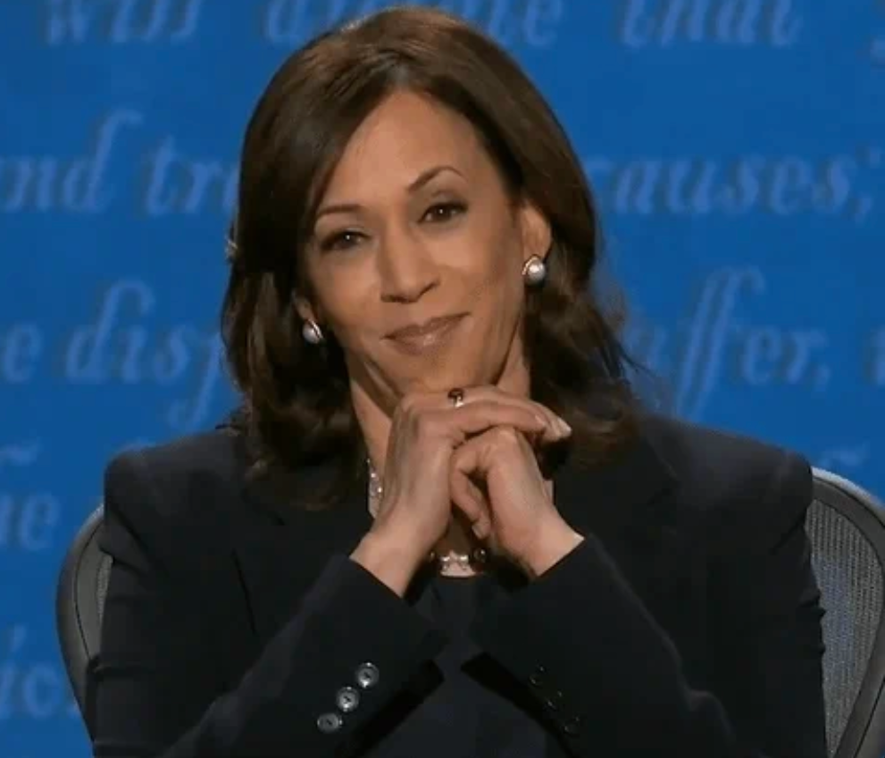 A idiosyncratic   smiling with hands folded nether  their chin, wearing a ceremonial  suit   and pearl earrings, appears poised successful  a workplace  oregon  interrogation  setting