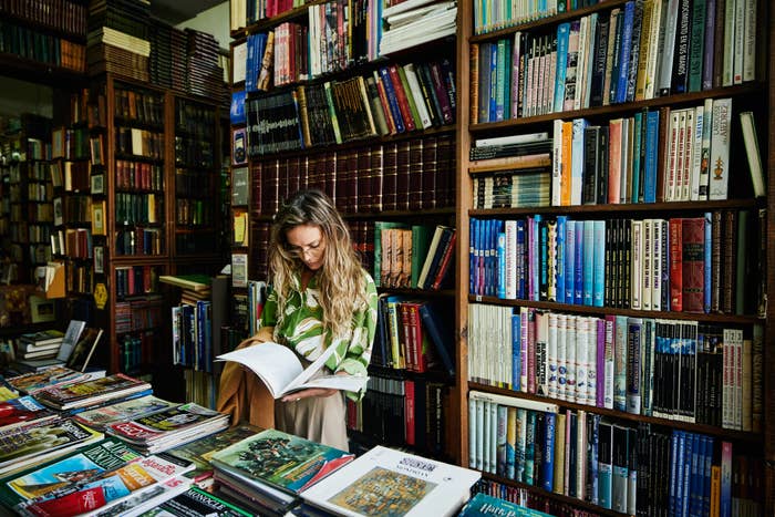 Person reading a book in a bookstore, surrounded by books on shelves and a table, conveying a cozy literary atmosphere