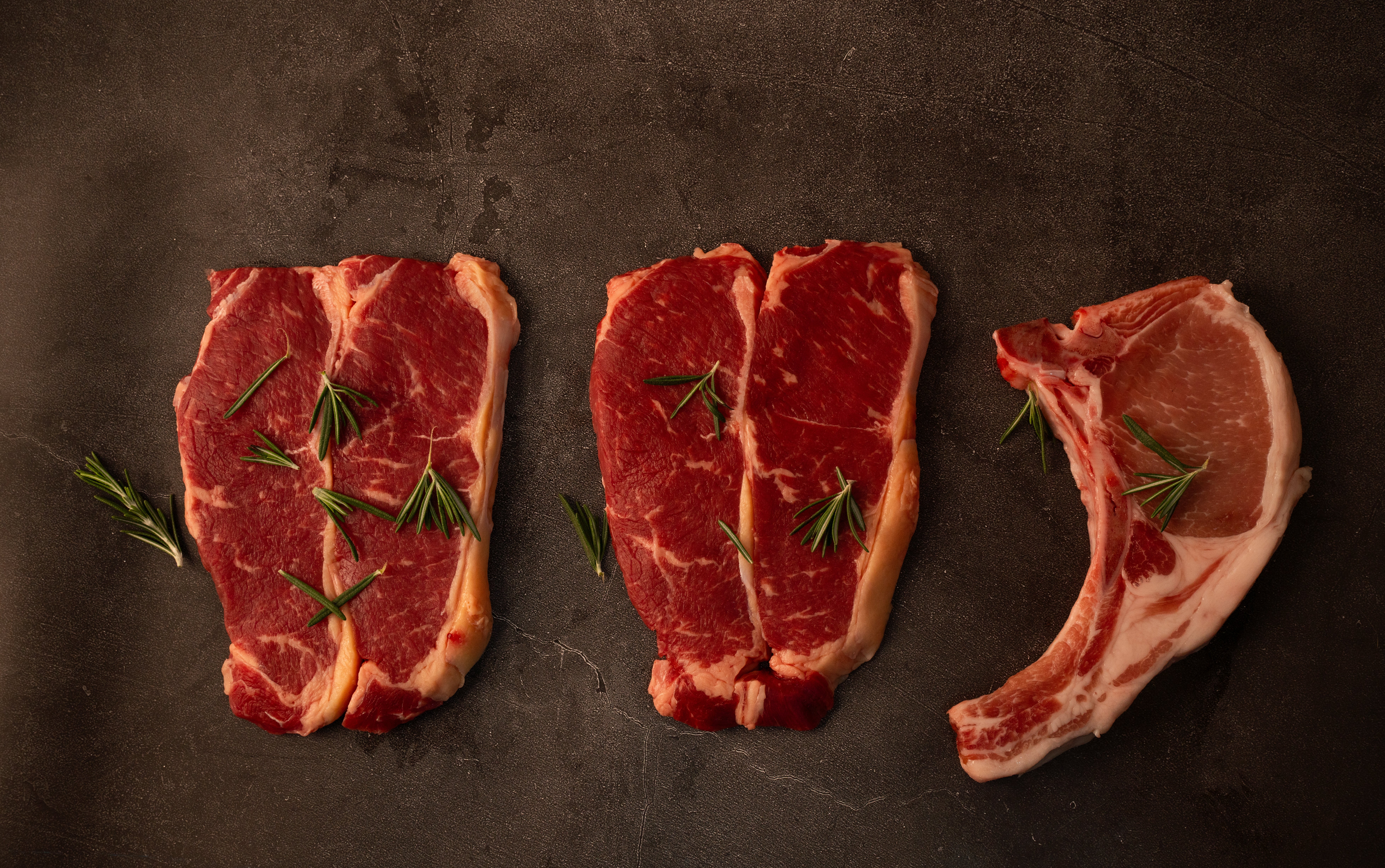 Three earthy   steaks connected  a acheronian  surface, garnished with sprigs of rosemary