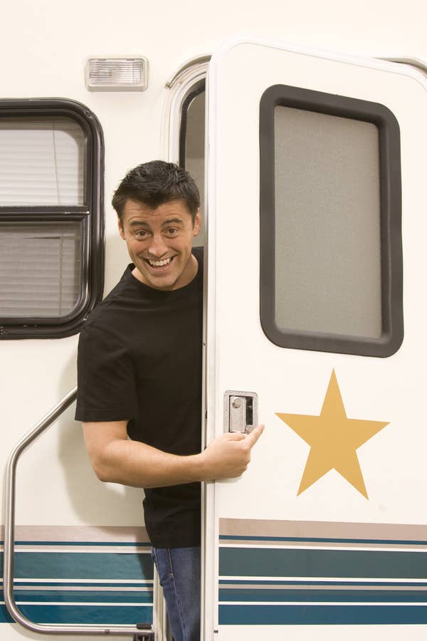 Matt LeBlanc smiling, standing in the open doorway of a trailer