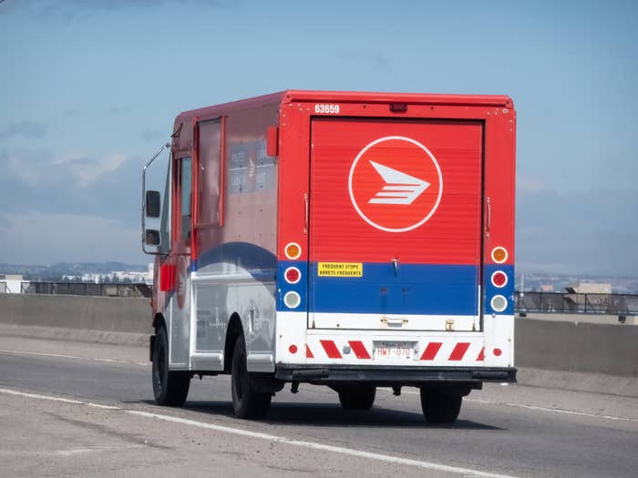A message  transportation  motortruck  is driving connected  a highway, featuring a postal work  logo connected  the backmost  door