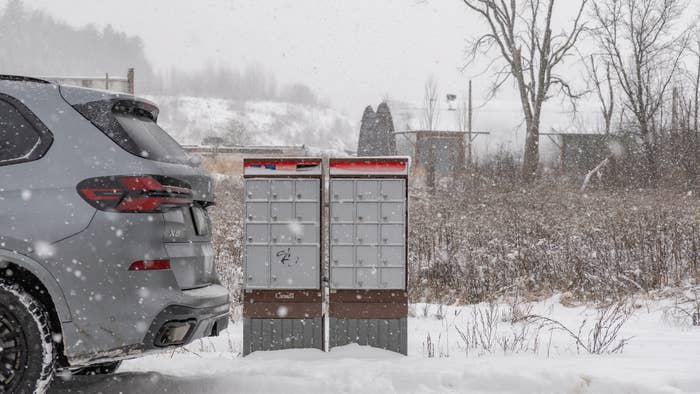 A car   parked adjacent   mailboxes successful  a snowy, agrarian  setting, with snowfall  falling and covering the crushed  and surrounding area