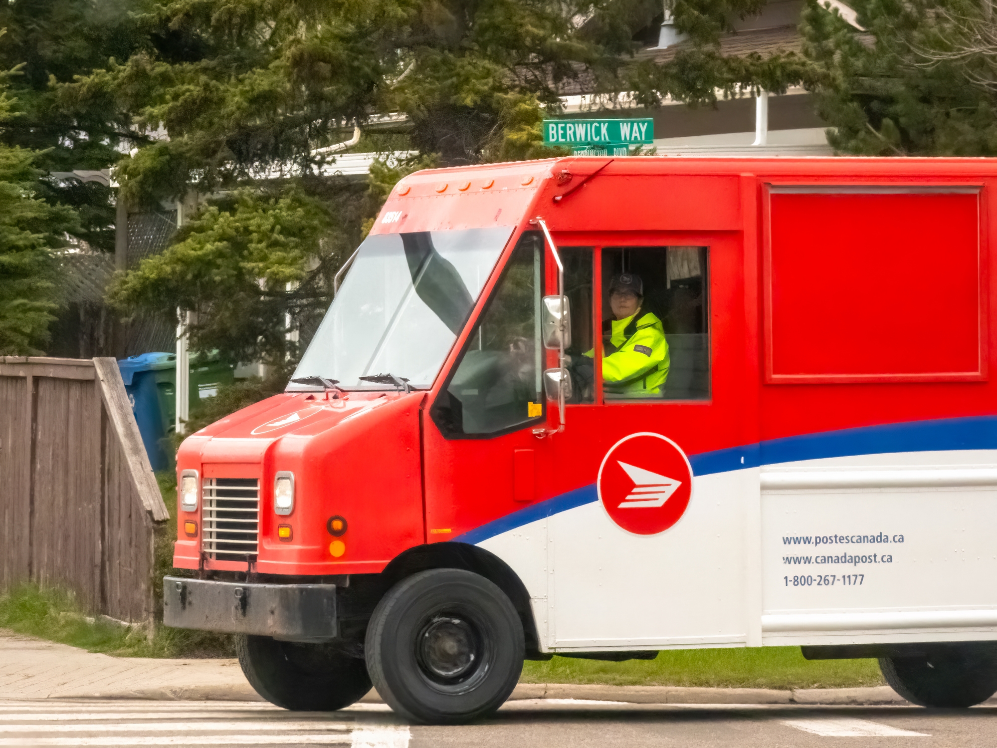 Postal motortruck  with operator  successful  uniform, parked connected  a suburban thoroughfare  adjacent   the intersection of Berwick Way