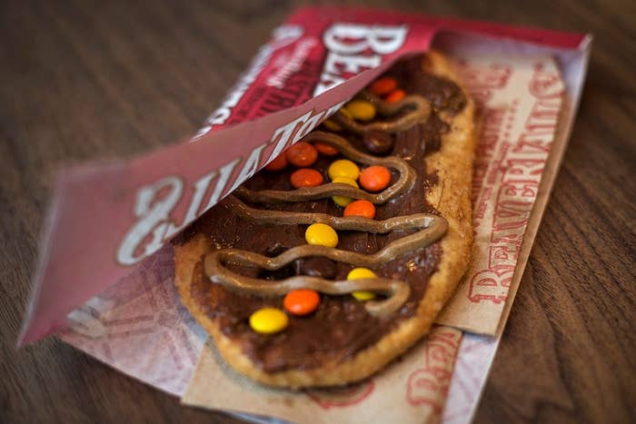 A flatbread dessert with cocoa  drizzle and colorful candy pieces partially wrapped successful  branded paper