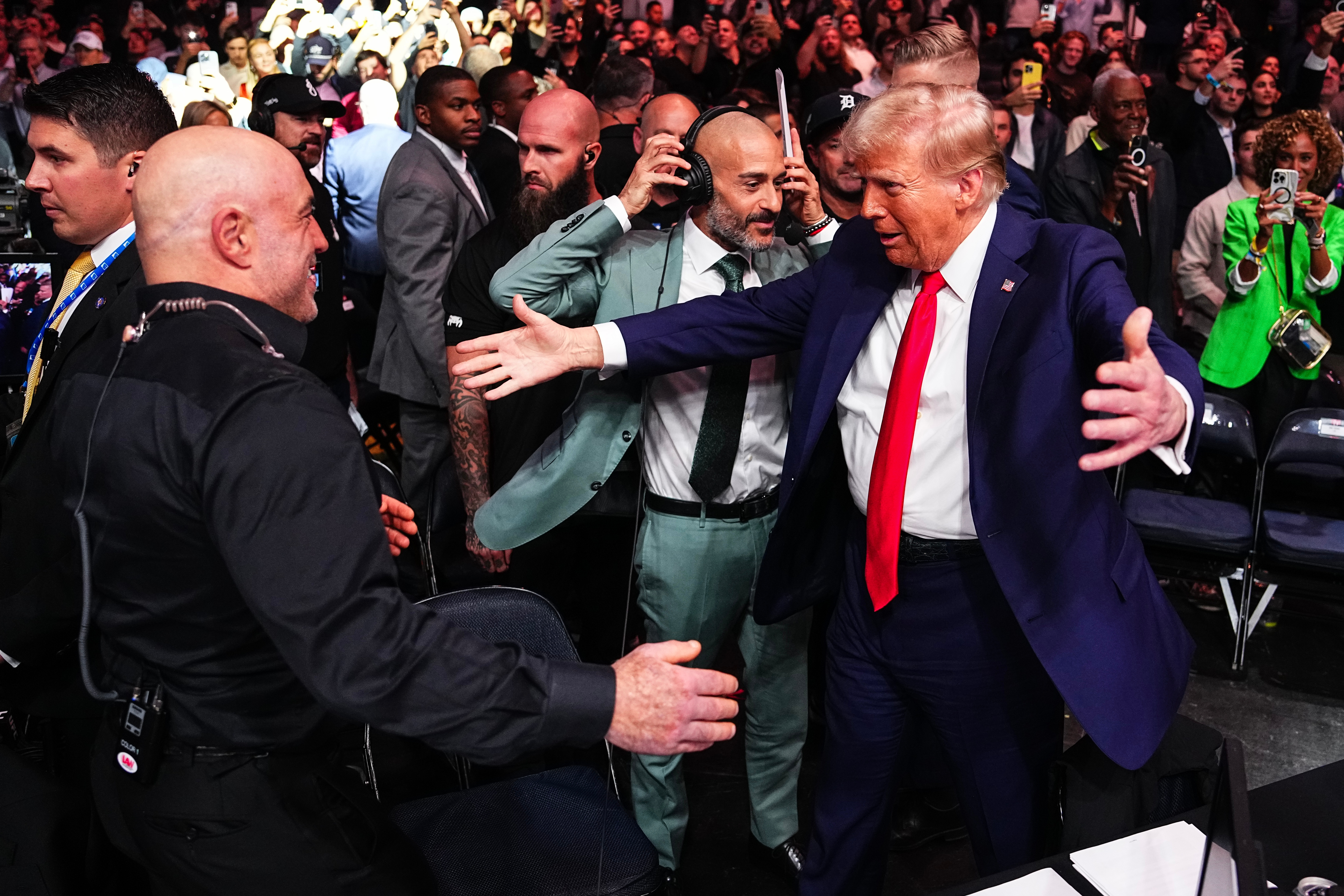 Two men successful  suits, surrounded by a crowd, widen  their arms for a handshake astatine  a lively event