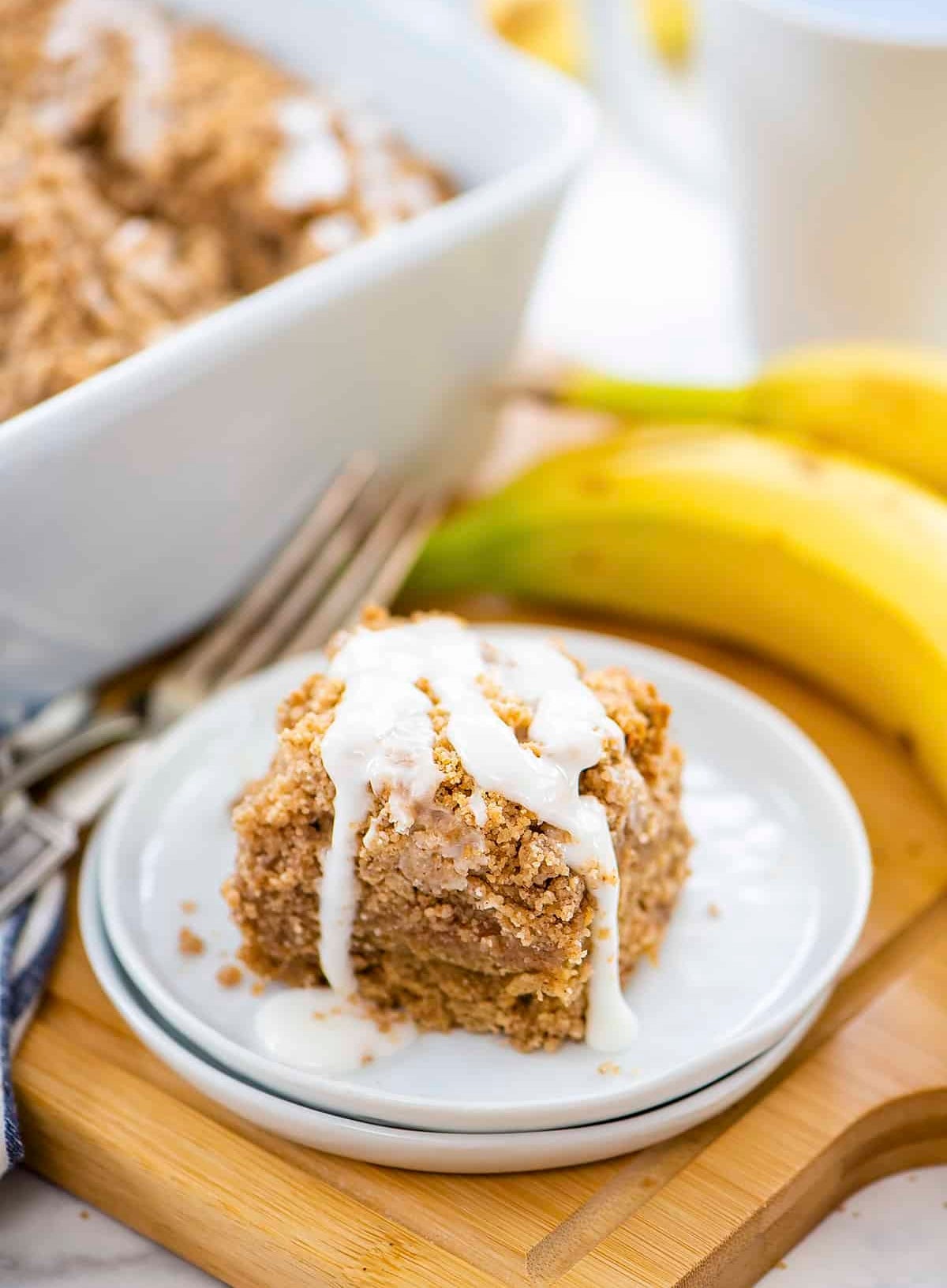 A portion of crumb barroom with icing connected a sheet adjacent to a clump of bananas and a cupful of coffee
