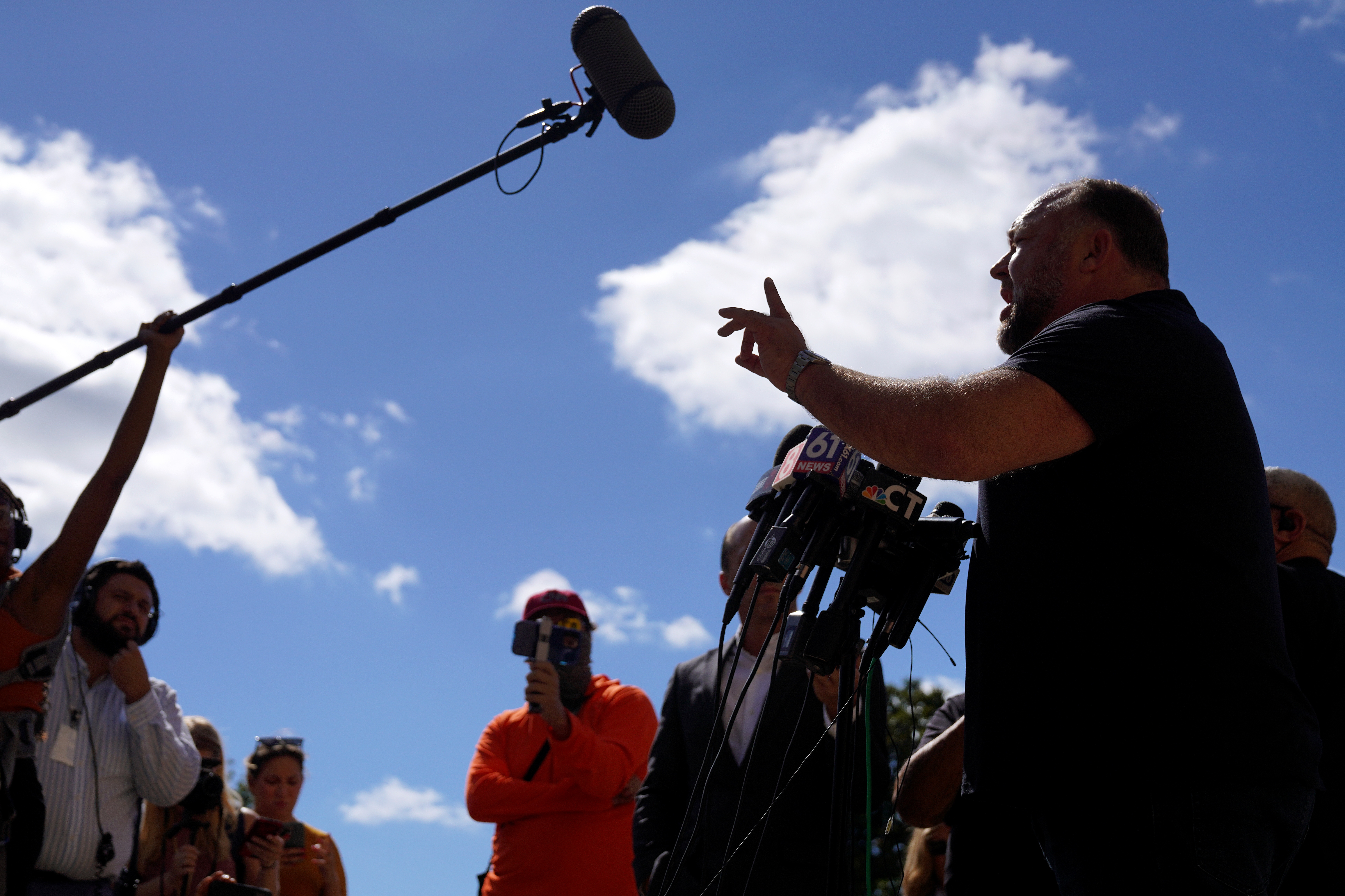 Person speaking passionately astatine  microphones outdoors, with onlookers and media capturing the moment