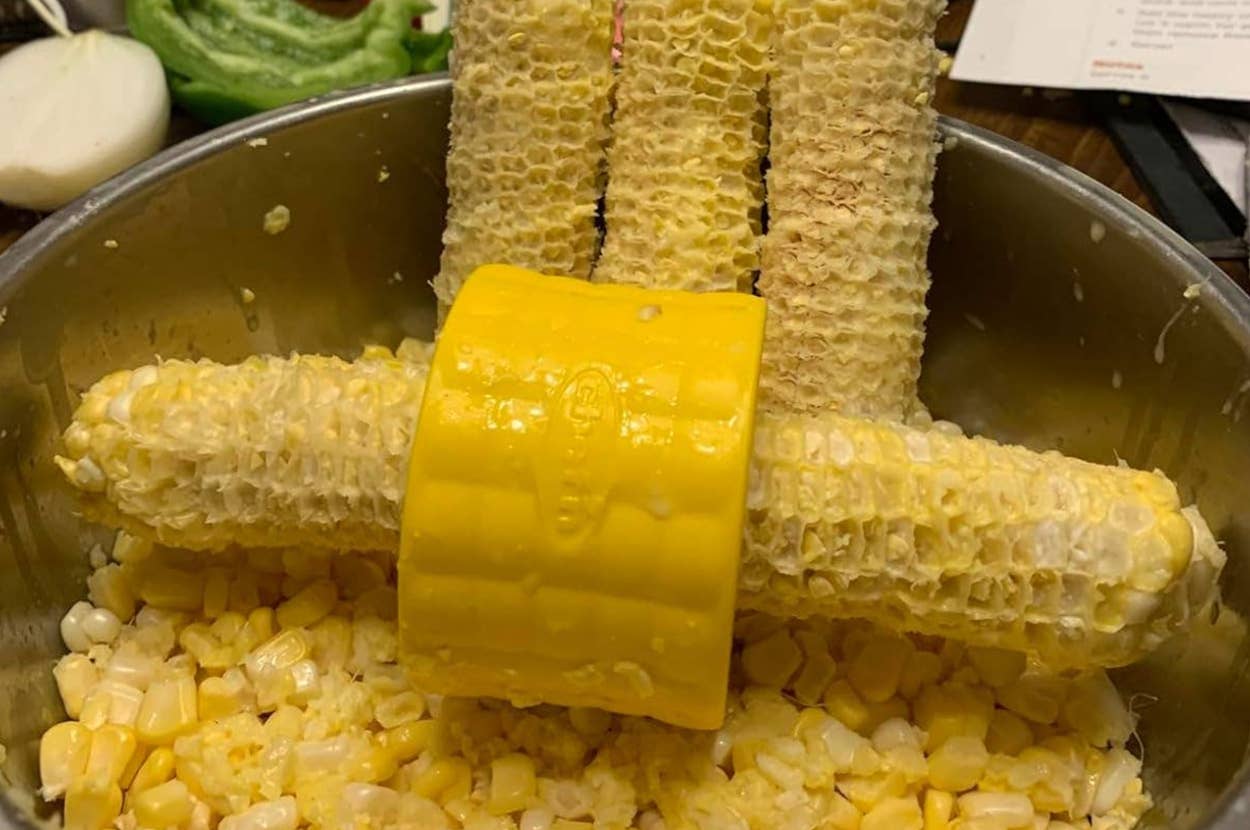 Corn being stripped with a yellow corn stripper, empty cobs over a bowl of kernels, onion and lettuce in the background