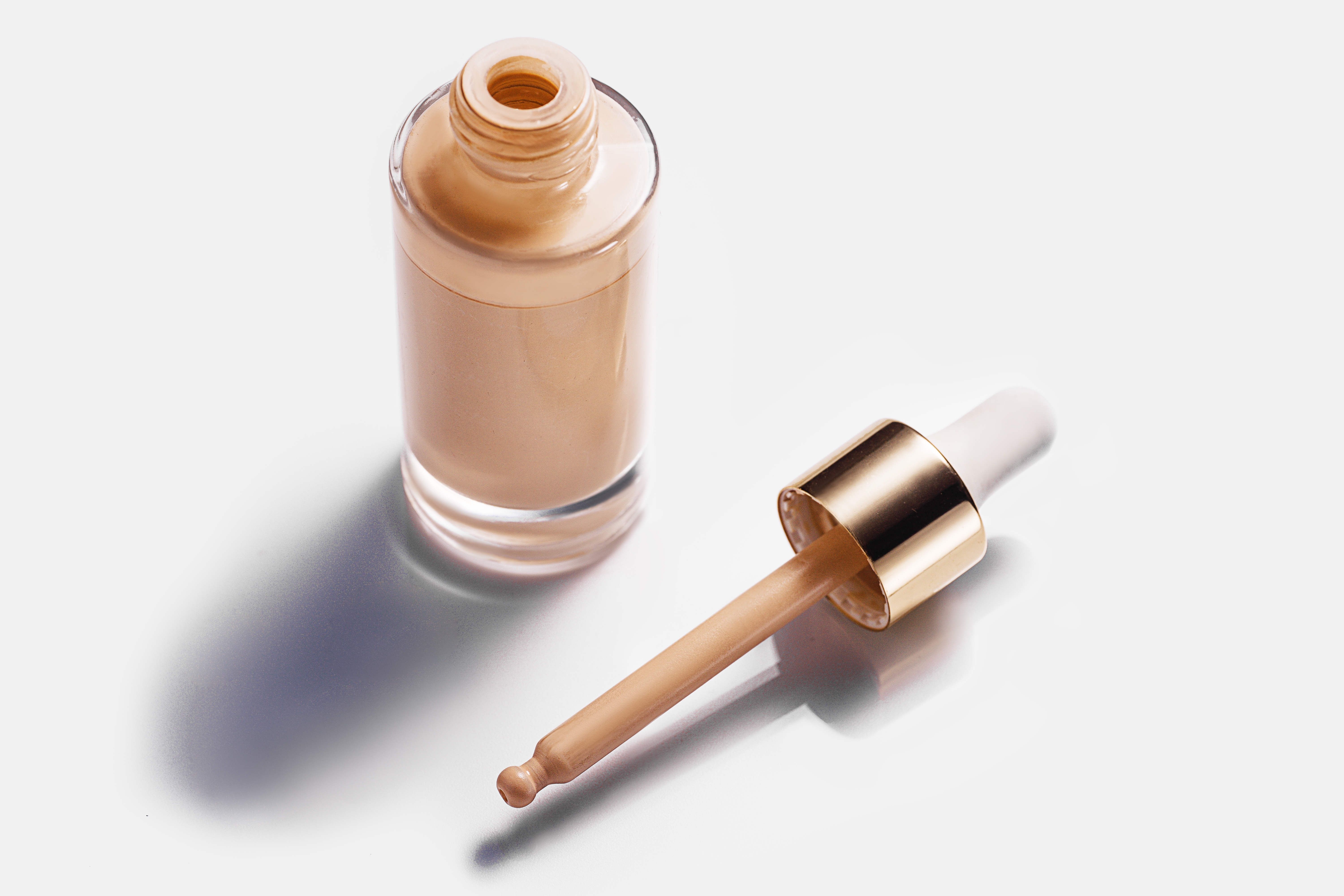 開いた瓶とスポイトに入ったリキッドファンデーションが白い背景に置かれている。