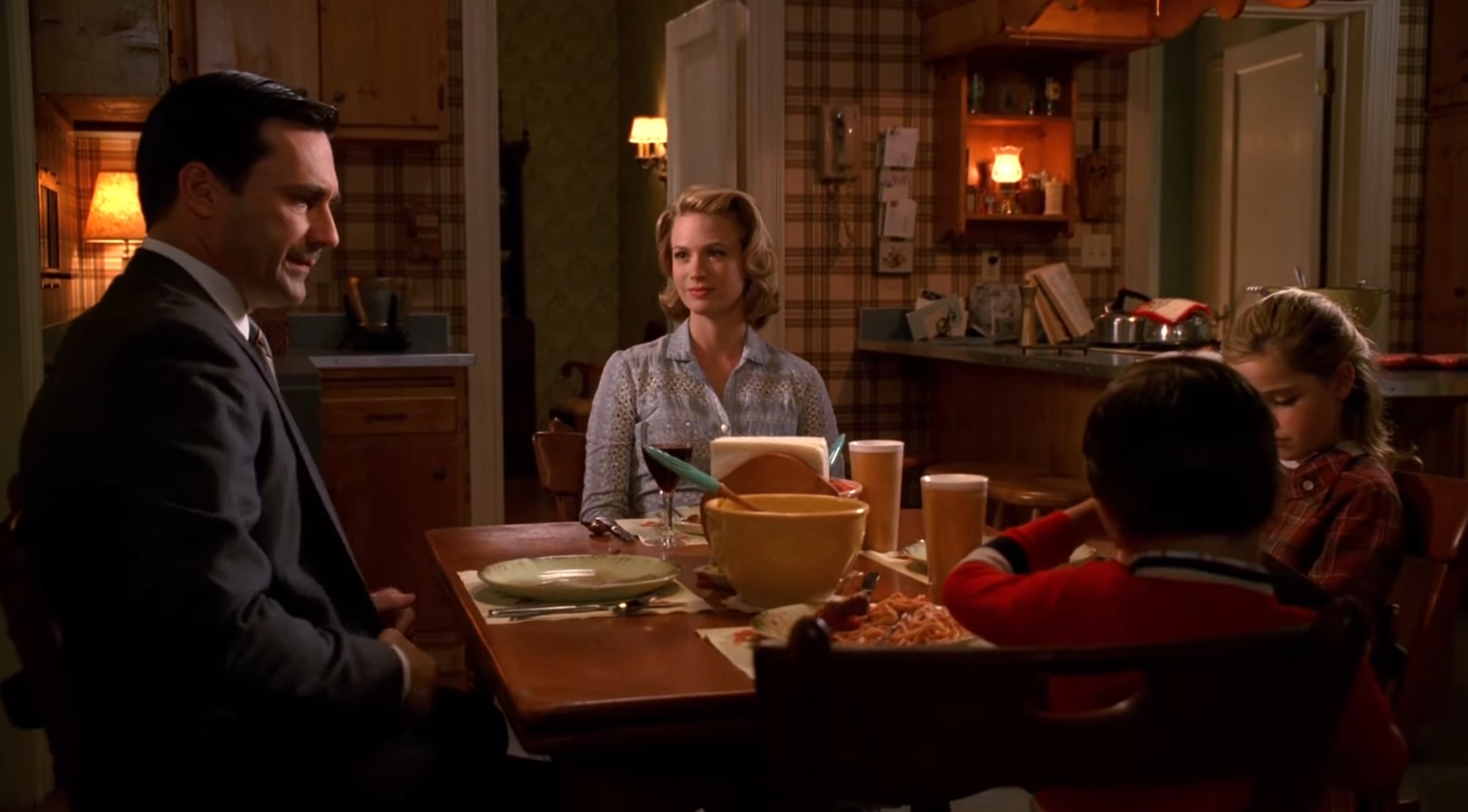 En familiescene fra 1960-tallet med voksne og barn som sitter ved et spisebord i en kjøkkensetting