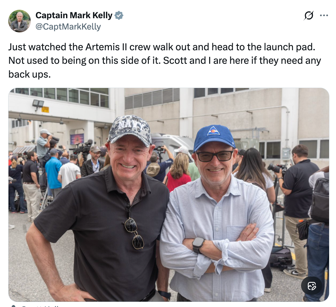 Two men, 1  wearing a achromatic  garment  and hat, the different   successful  a bluish  headdress  and button-down shirt, basal   smiling extracurricular  a building, with radical   successful  the background