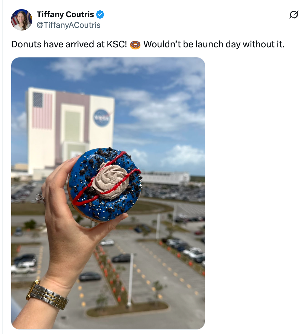A manus  holds a space-themed donut successful  beforehand   of a NASA building, celebrating motorboat  time  astatine  Kennedy Space Center