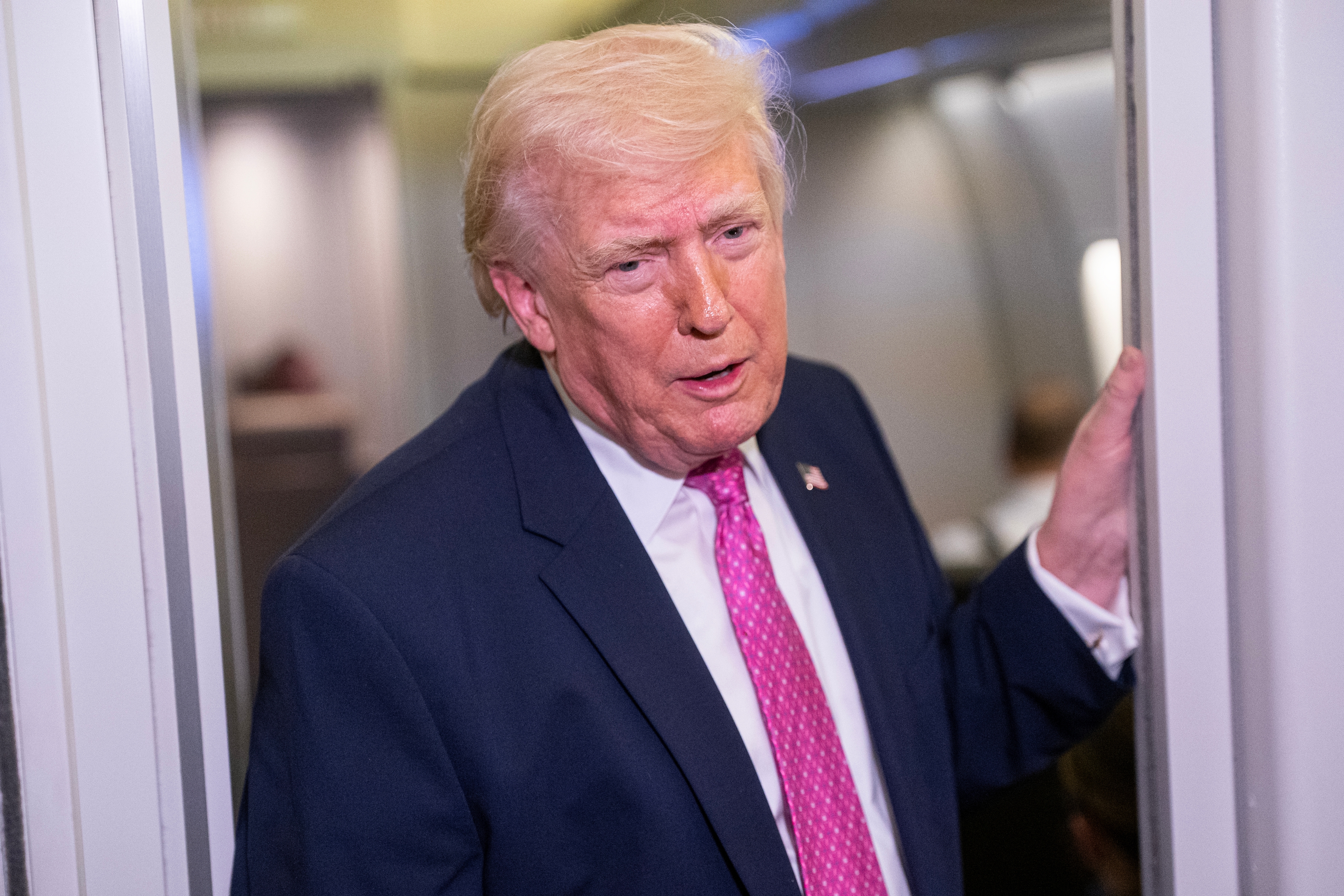 Man successful  a suit   with a pinkish  necktie  stands successful  an airplane aisle, speaking