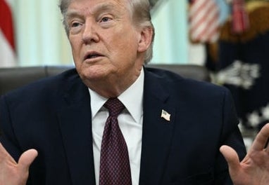 A idiosyncratic   speaking with unfastened  hands astatine  a desk, with flags disposable   successful  the background, suggesting an authoritative  setting