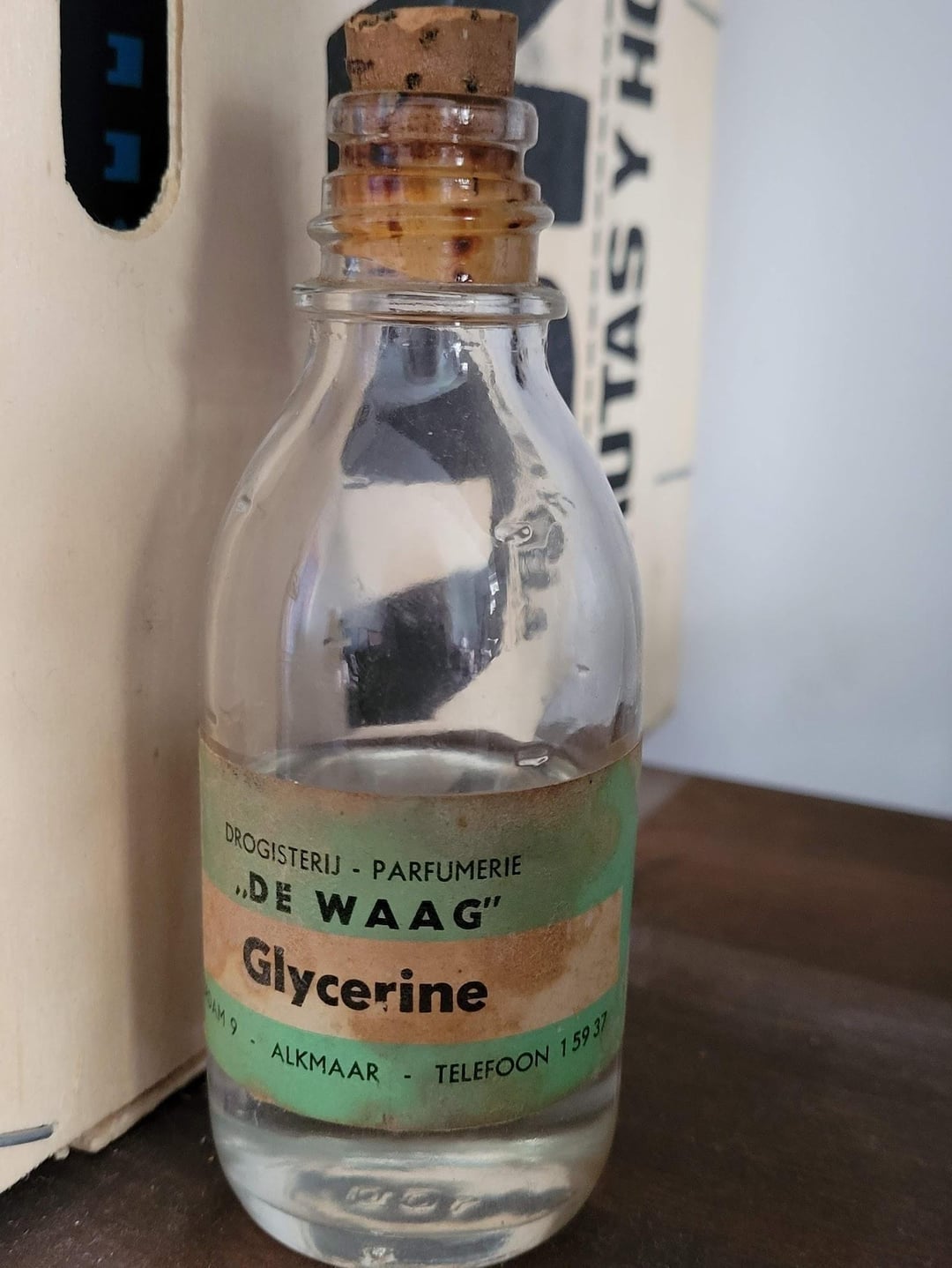 A vintage vessel  of glycerine with a cork stopper and a statement   from "De Waag" perfumery, placed connected  a woody  surface