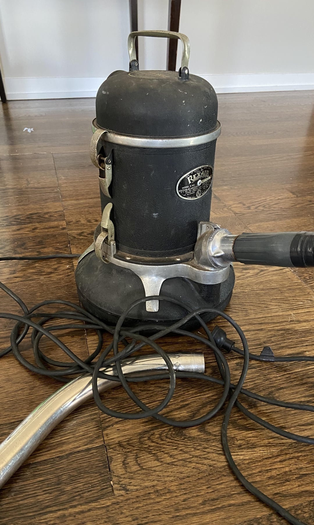 Vintage vacuum cleaner with metallic  detailing and a achromatic  assemblage  sits connected  a woody  level  with its cord and hose successful  view