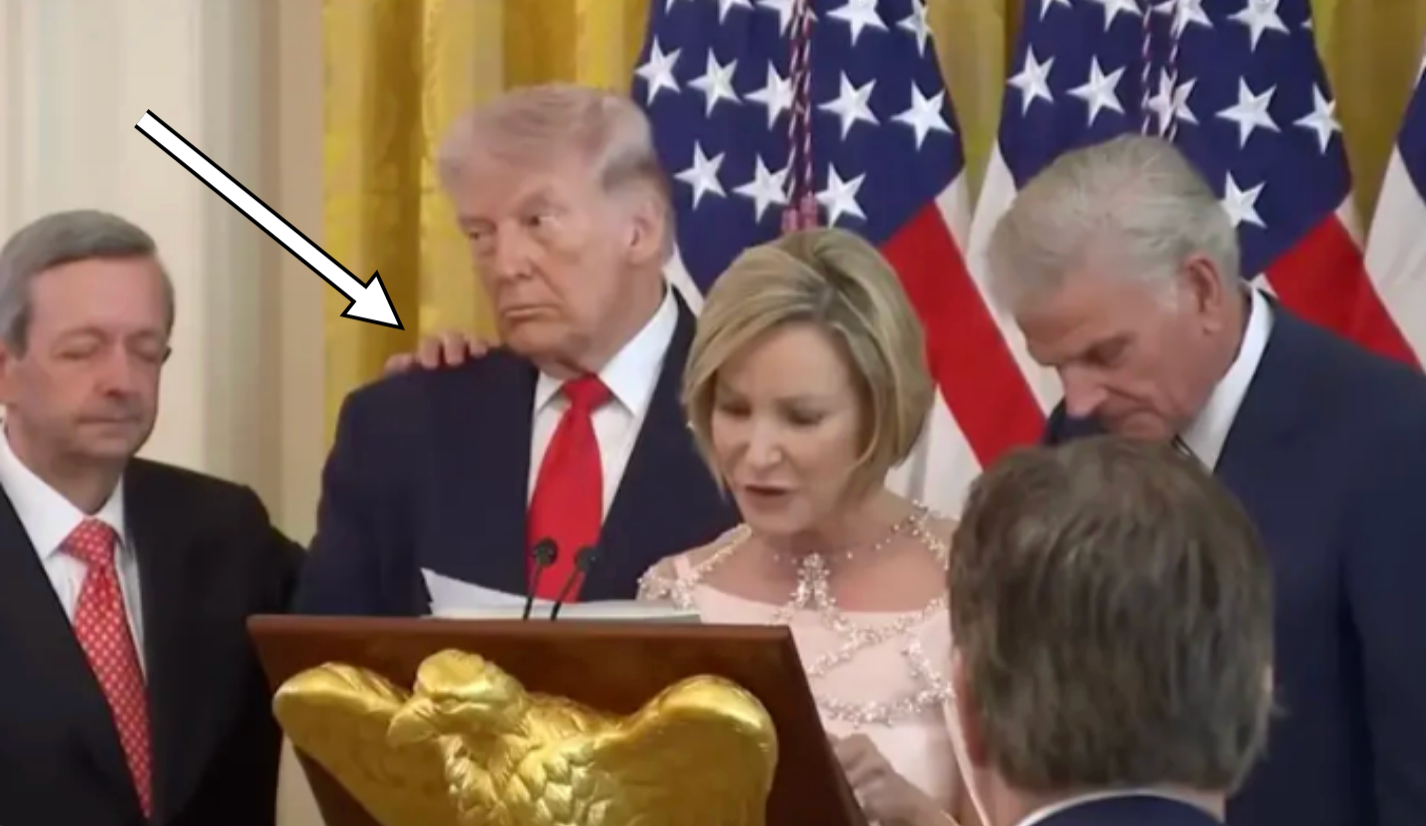 En gruppe mennesker står høytidelig ved et podium med flagg i bakgrunnen under det som ser ut til å være en formell begivenhet