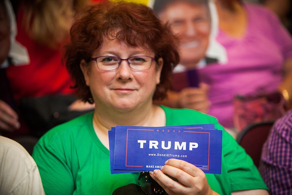 En person holder Trump-kampanjefoldere på et arrangement, med et papputklipp av en person i bakgrunnen