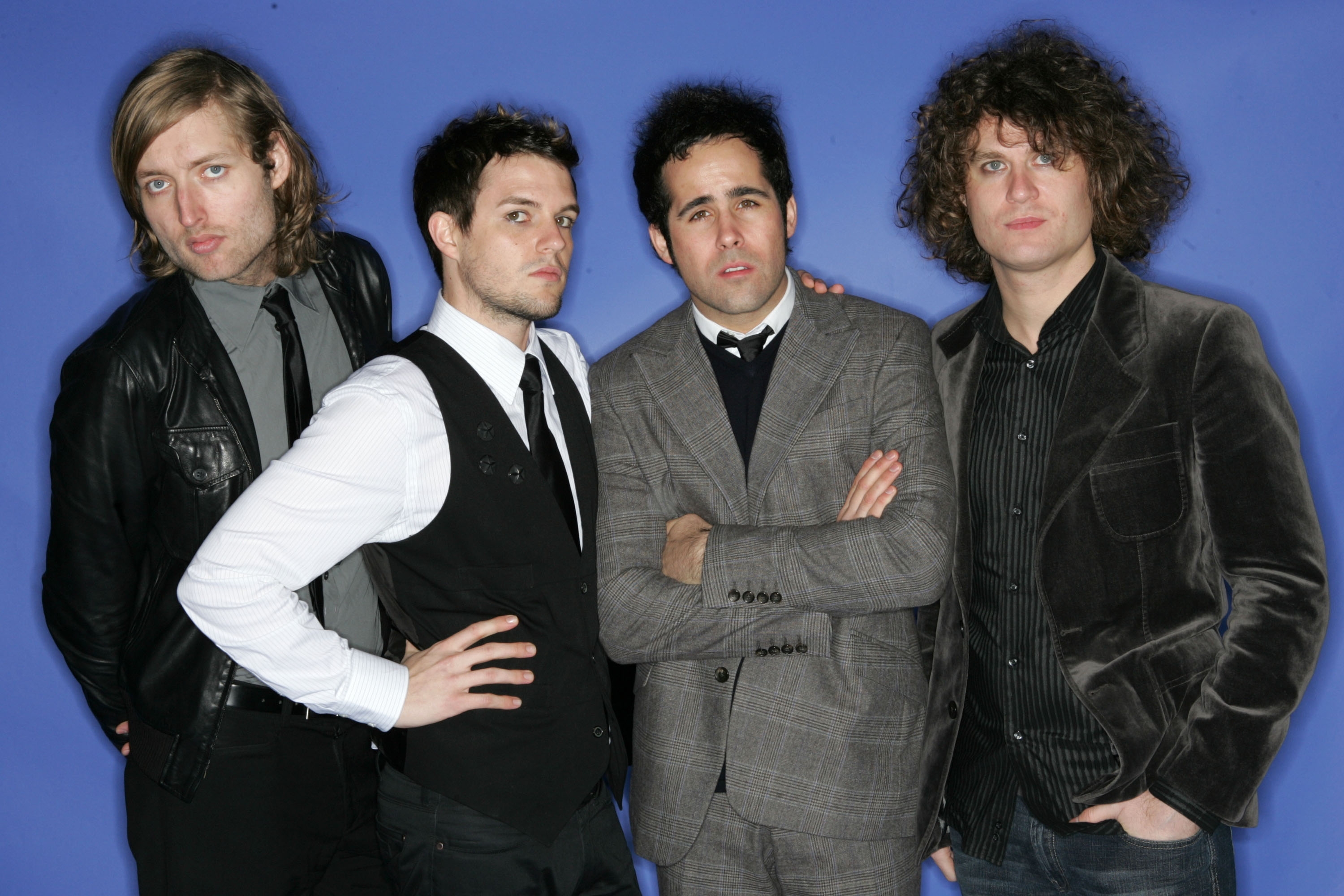 Four men posing; 3  successful  suits, 1  successful  a leather jacket, and 1  with curly hairsbreadth  successful  a velvet blazer