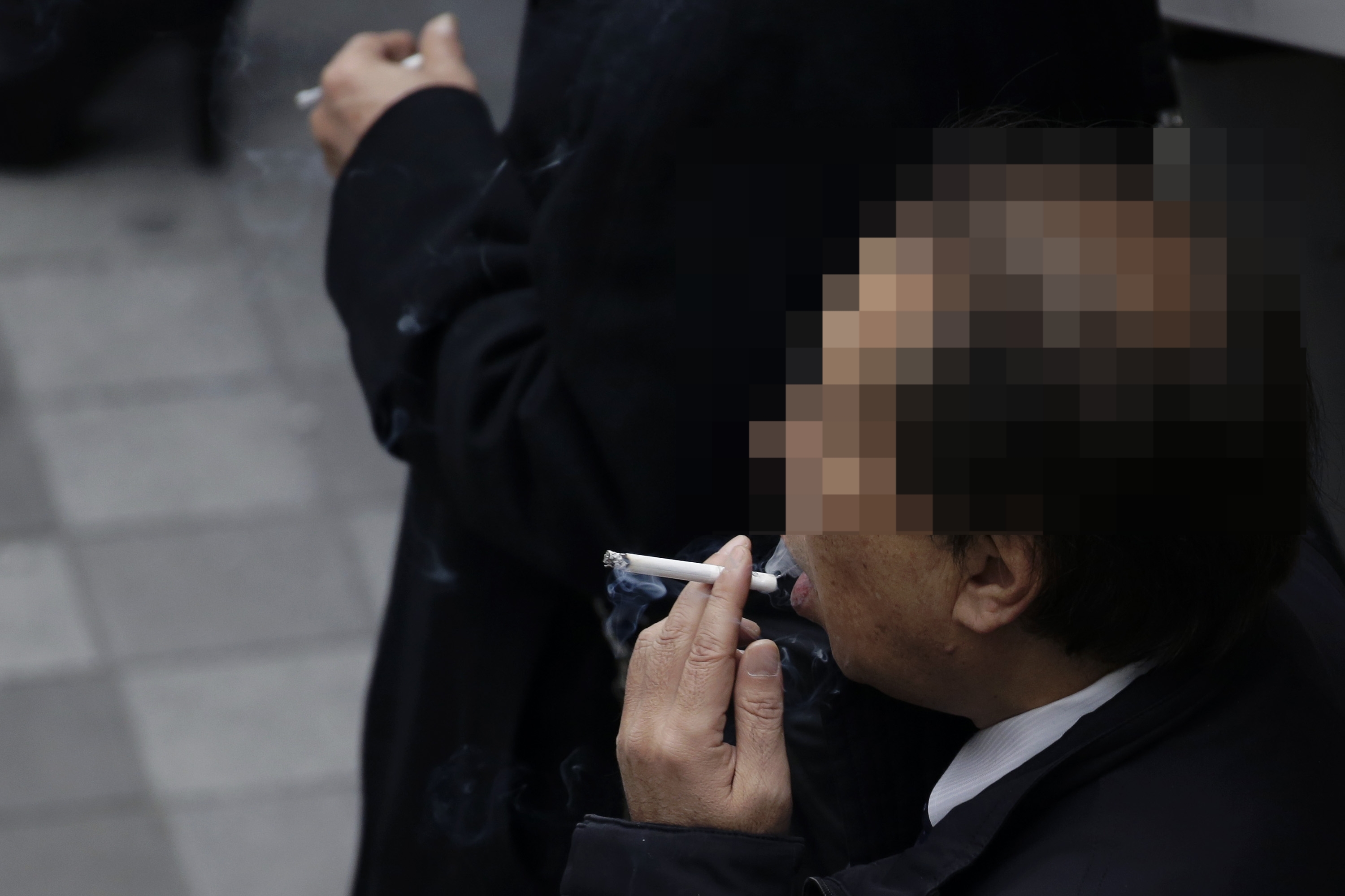 Two radical   successful  coats are smoking portion    lasting  connected  a sidewalk. The absorption   is connected  a idiosyncratic   taking a resistance  from a cigarette