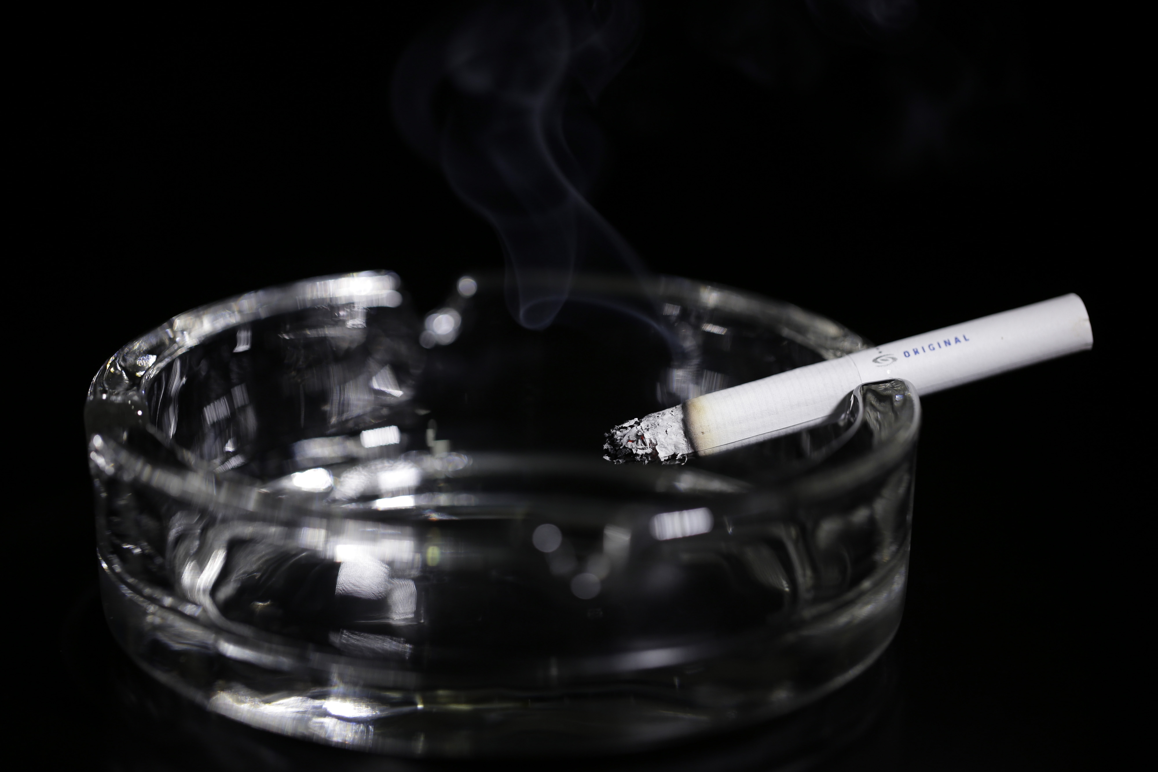 Lit cigaret  resting connected  a wide   ashtray with disposable   fume  rising