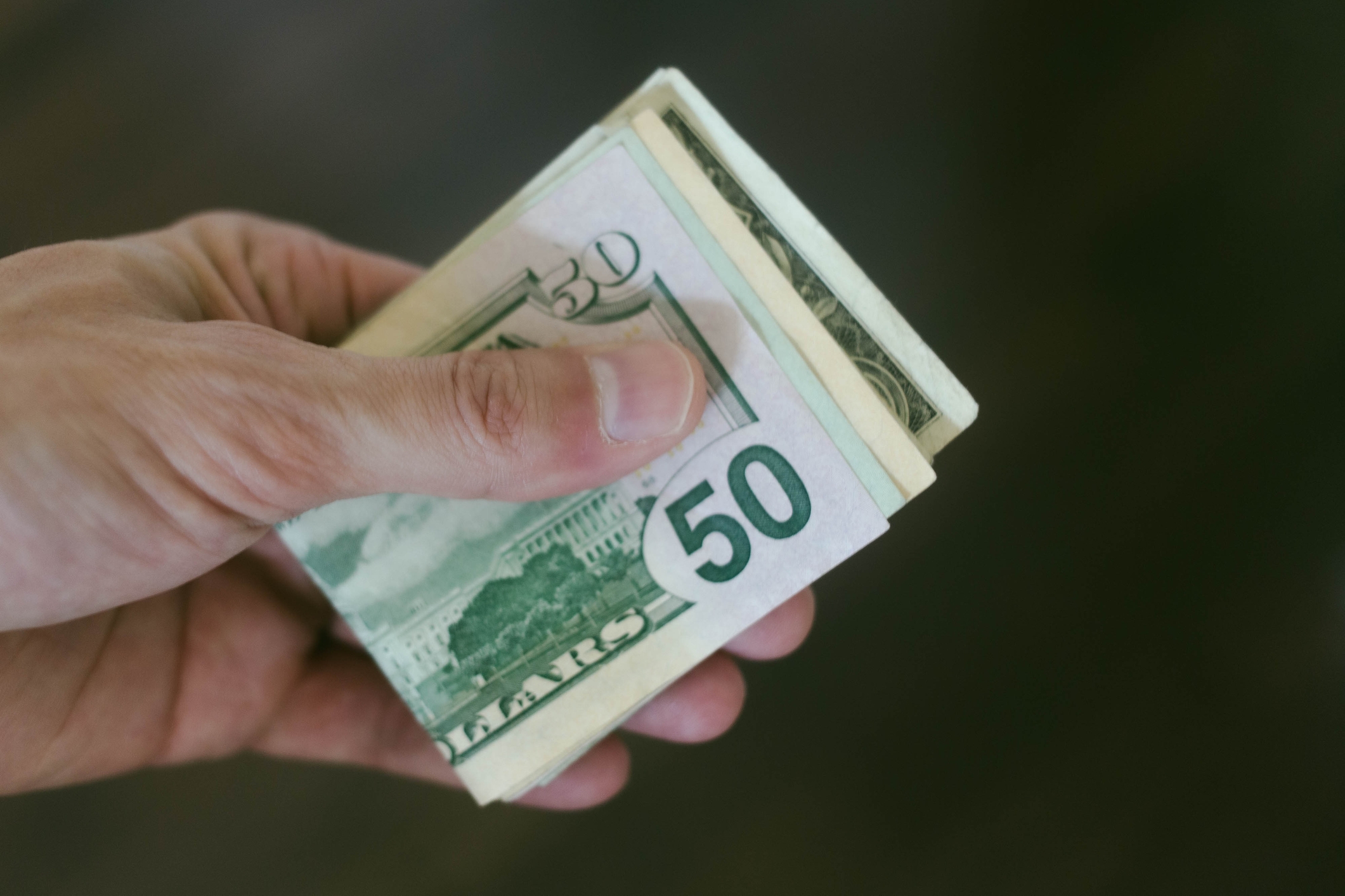 A manus holding a stack of 50 dollar bills, suggesting a monetary transaction oregon payment