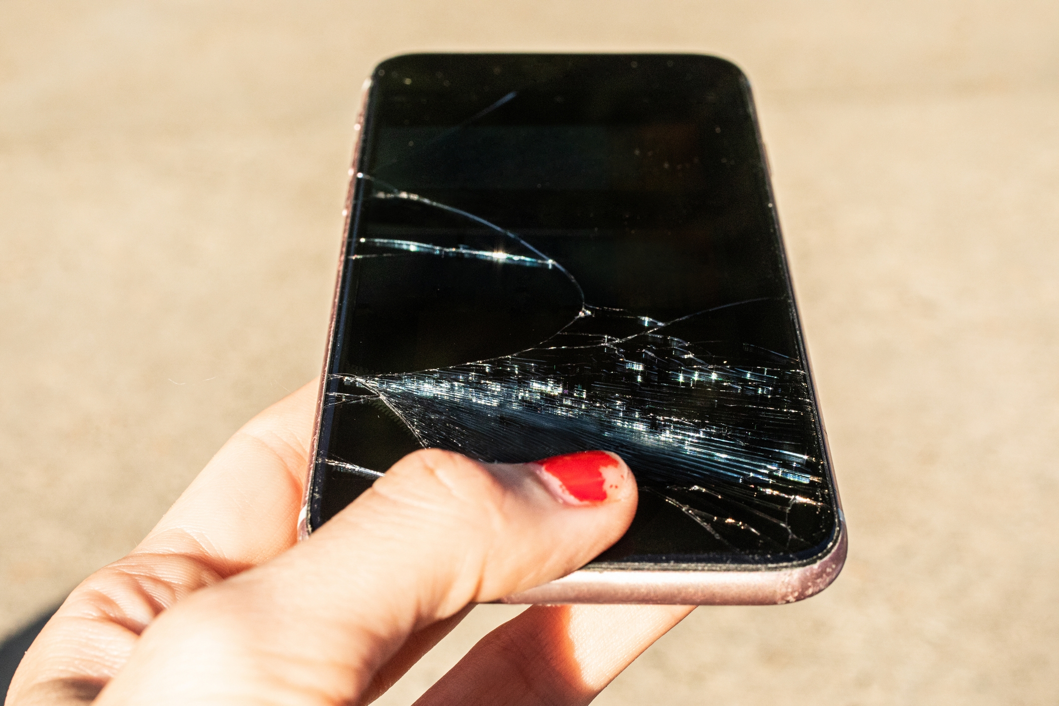 Person holding a smartphone with a cracked screen