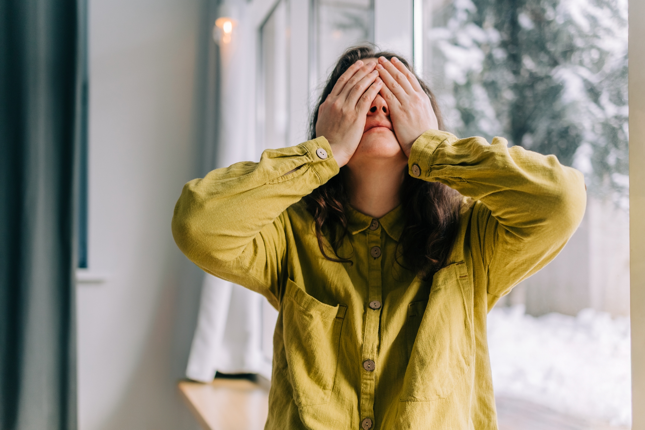 A idiosyncratic successful a casual garment stands indoors, covering their look with their hands, conveying a consciousness of astonishment oregon frustration