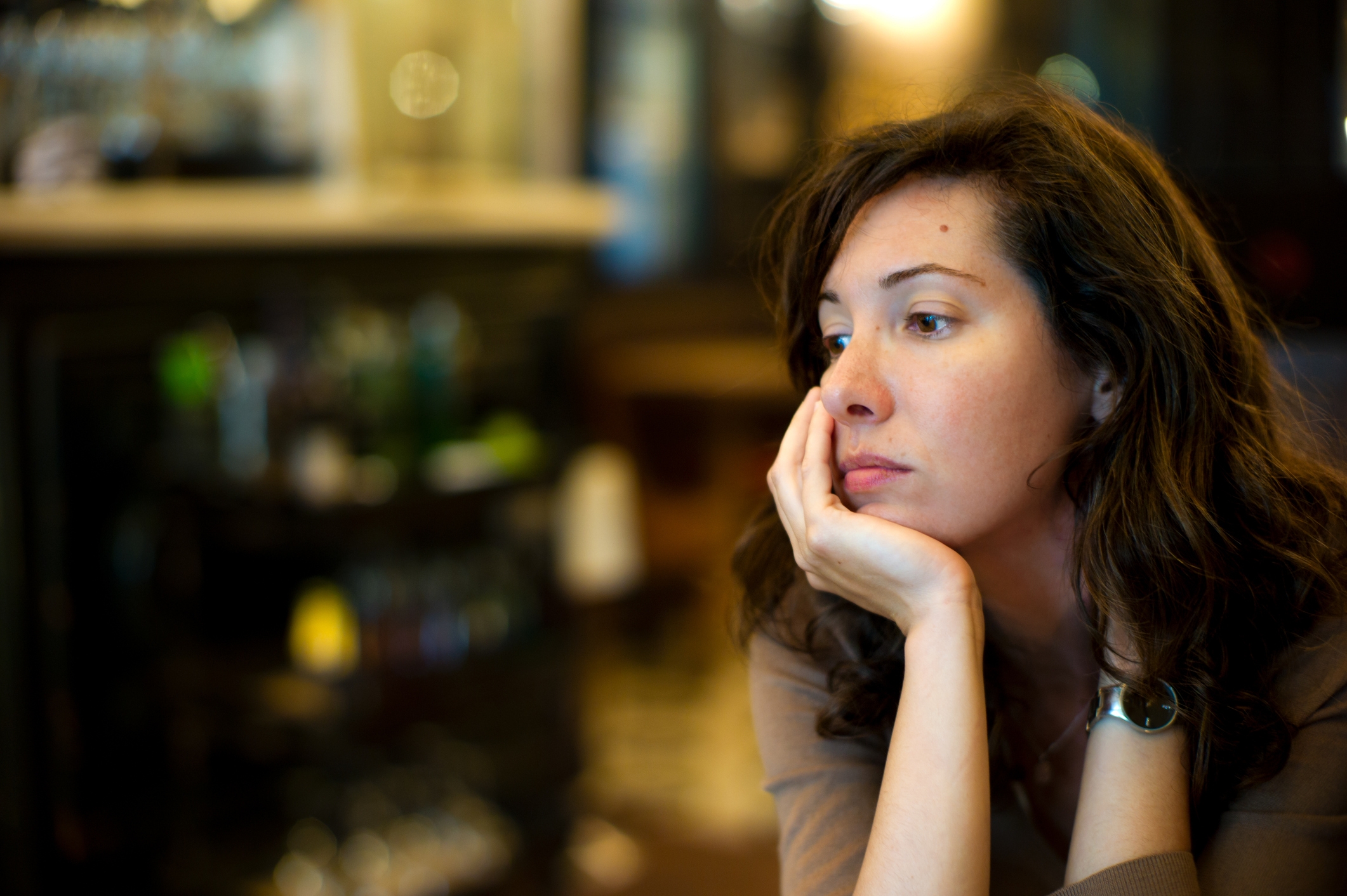 Person with wavy hairsbreadth successful a thoughtful pose, resting chin connected manus astatine a cafe, with a blurry background