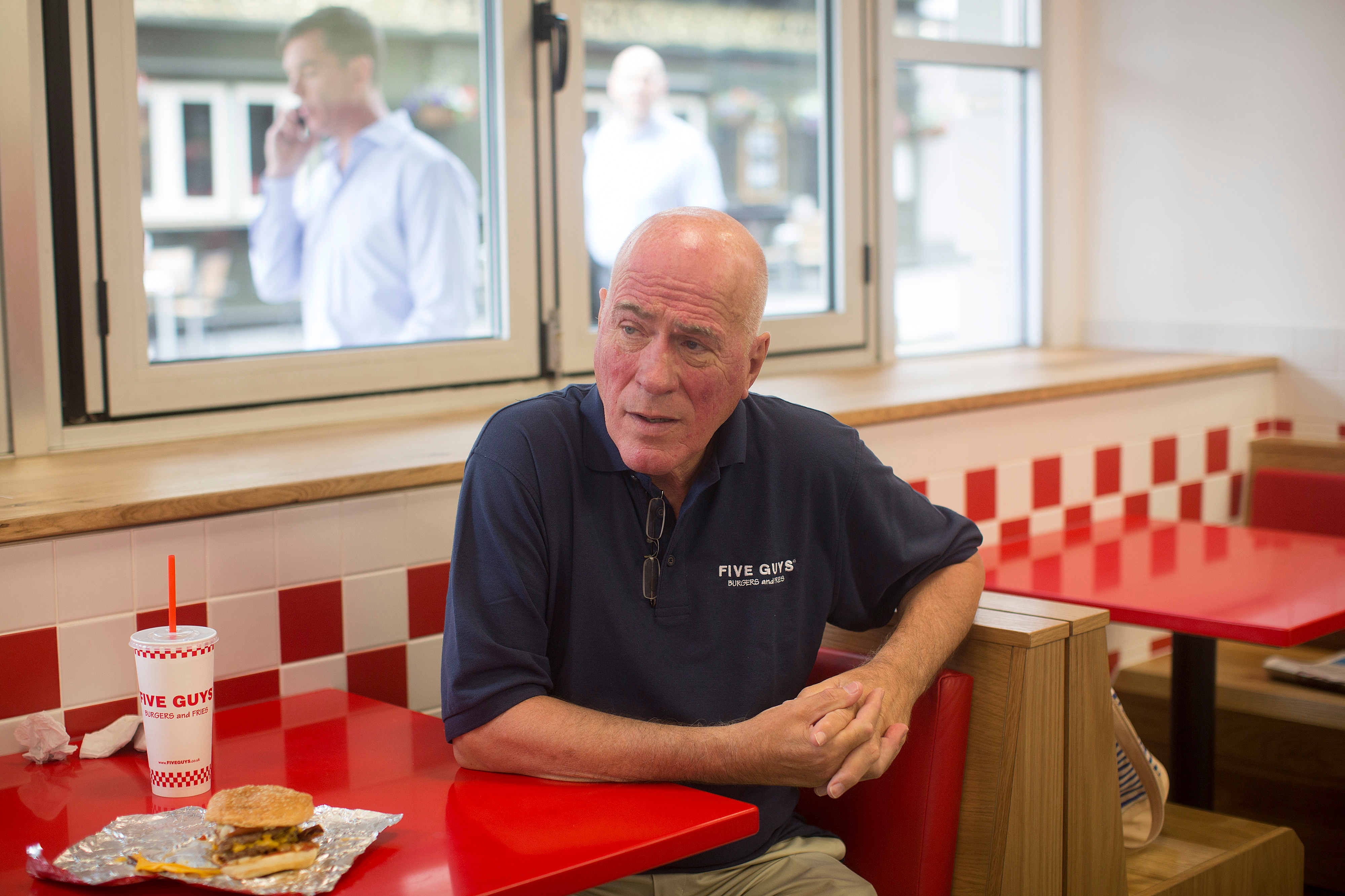Man sitting astatine  a Five Guys edifice  array  with a burger and drink; 2  radical   disposable   extracurricular  model   successful  background