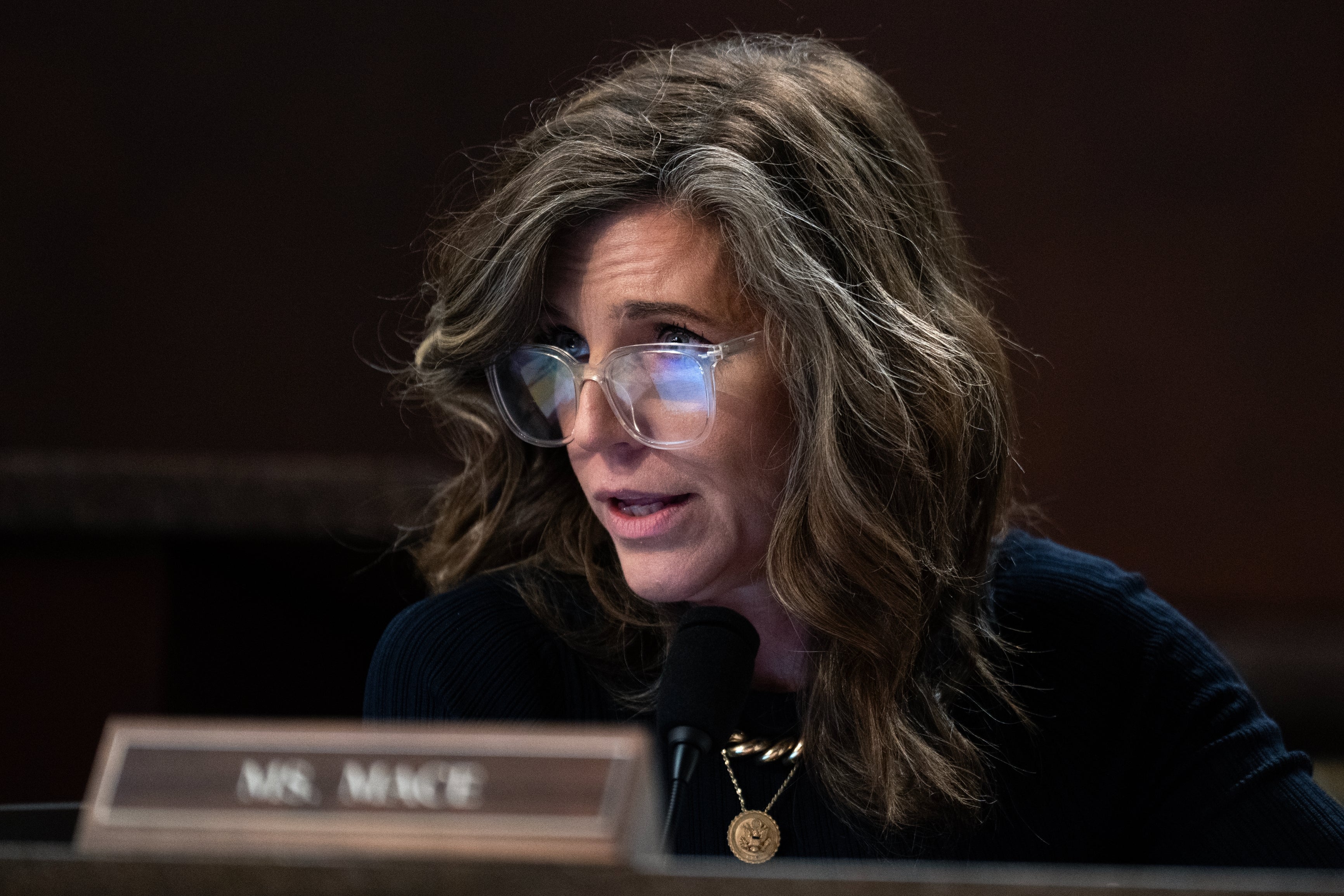 Nancy Mace med bølget hår og briller snakker inn i en mikrofon på en formell begivenhet. Navneskilt synlig