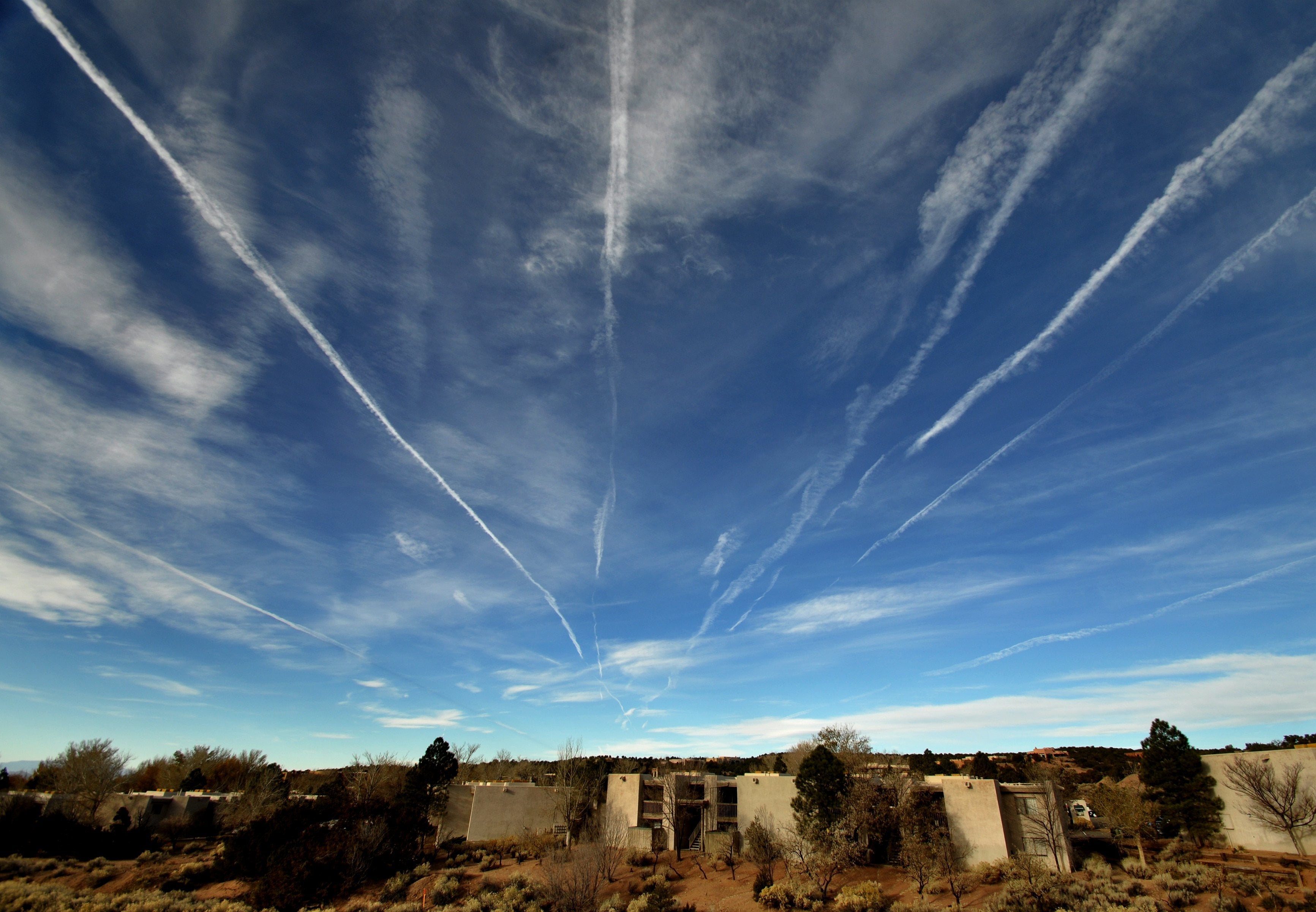 Ørkenlandskap med gamle strukturer og mange linjer som strekker seg over himmelen, noe som tyder på aktiv flytrafikk