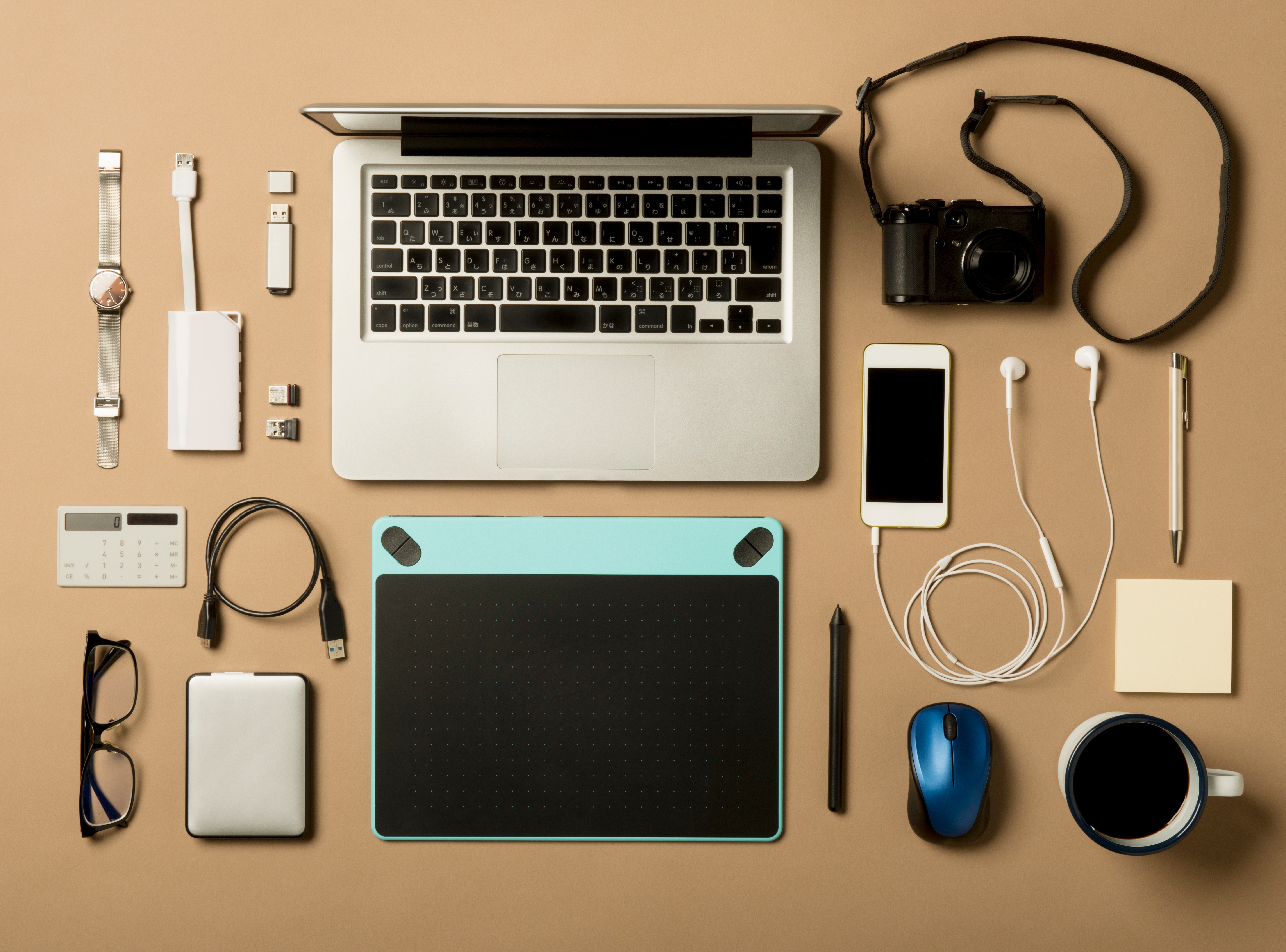 デスクに置かれたノートパソコン、カメラ、スマホ、イヤホン、タブレット、メガネ、マウス、USBなどのガジェットとアクセサリー。